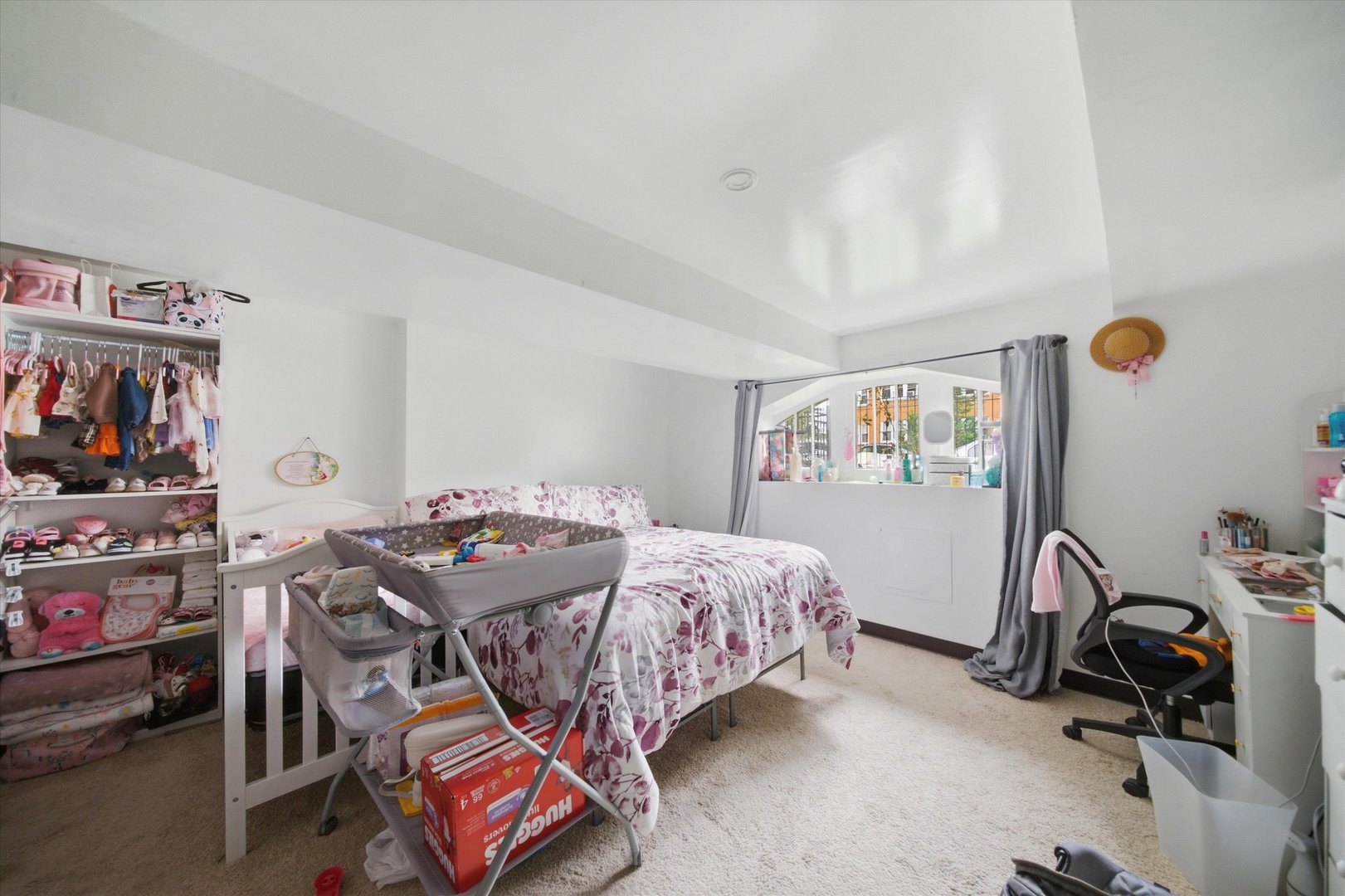 Bedroom with a floral bed, crib, and shelves of children’s clothes and shoes.