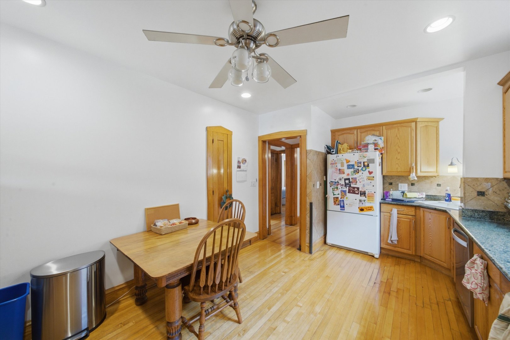 Kitchen with honey-colored cabinets, a magnet-covered refrigerator, granite counters, and an adjoining wooden dining table.