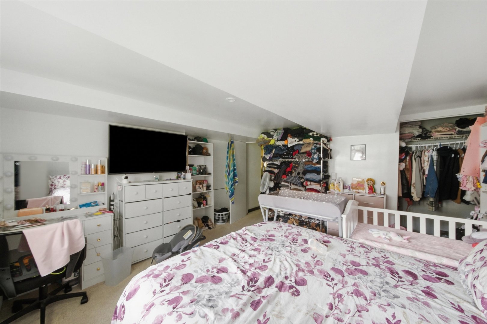Bedroom with floral bedding, a crib, a large television, and open clothing storage.