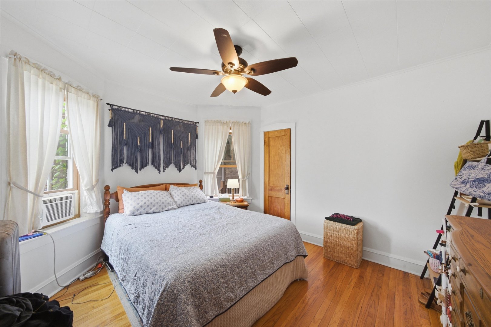 Furnished bedroom with a large bed, hardwood floors, and a ceiling fan.