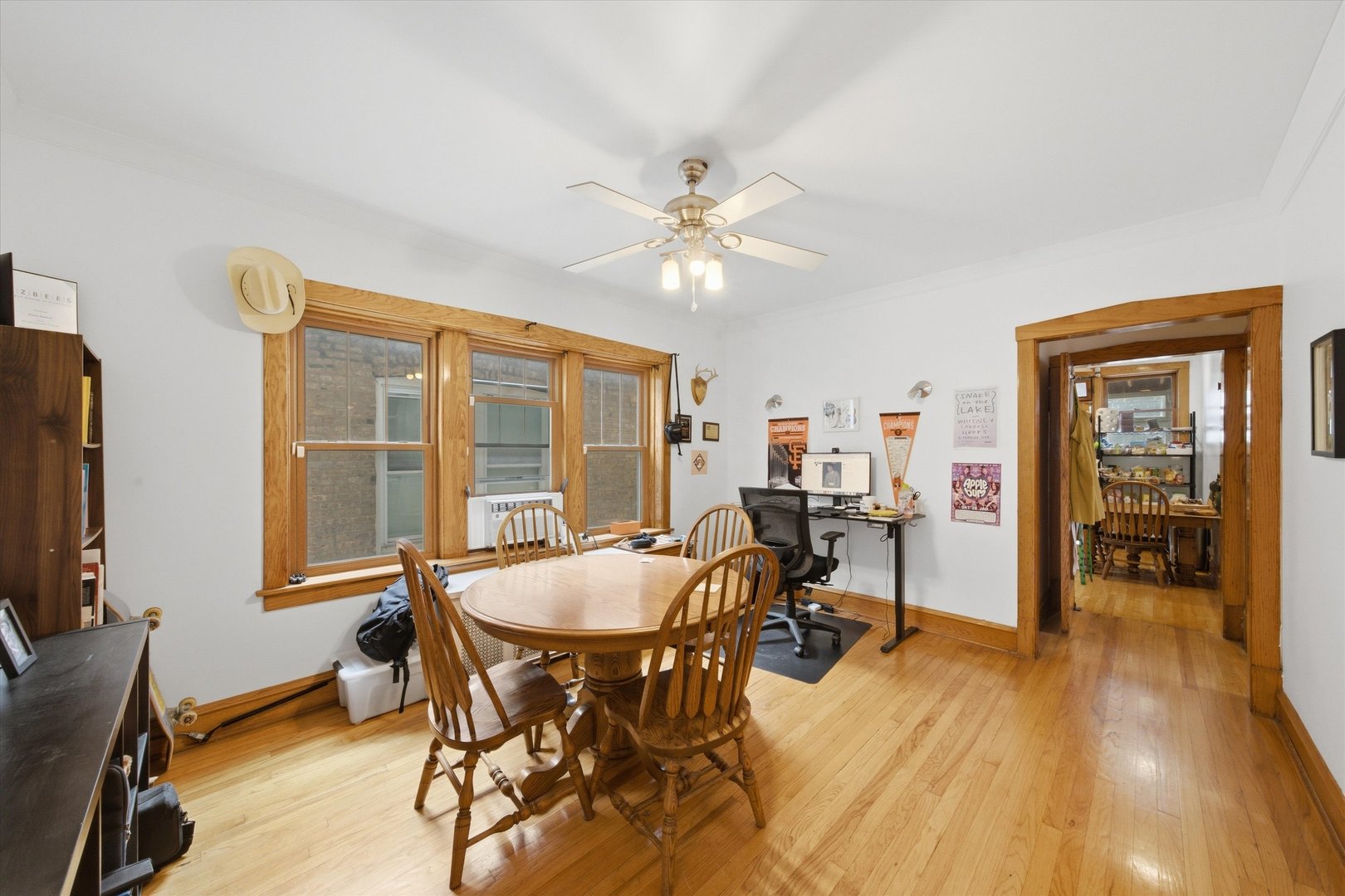 Dining room with a round wooden table, hardwood floors, and a desk beneath wood-trimmed windows.
