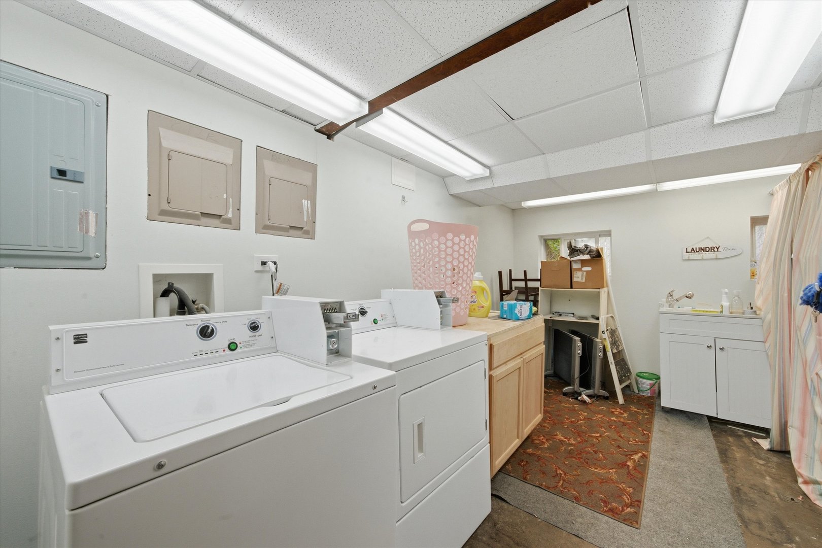 Laundry room with multiple washers and dryers, a utility sink, and a patterned rug.