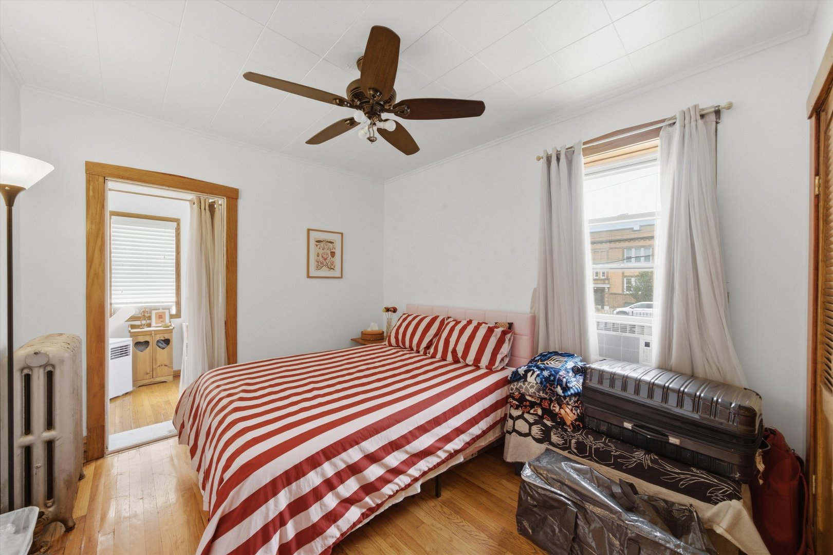 Bedroom with red-and-white striped bedding, hardwood floors, and a dark ceiling fan.
