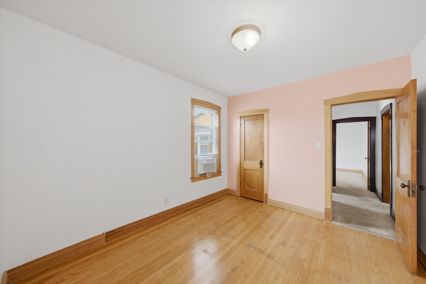 Empty room with hardwood floors, a pale pink wall, and a window air conditioner.