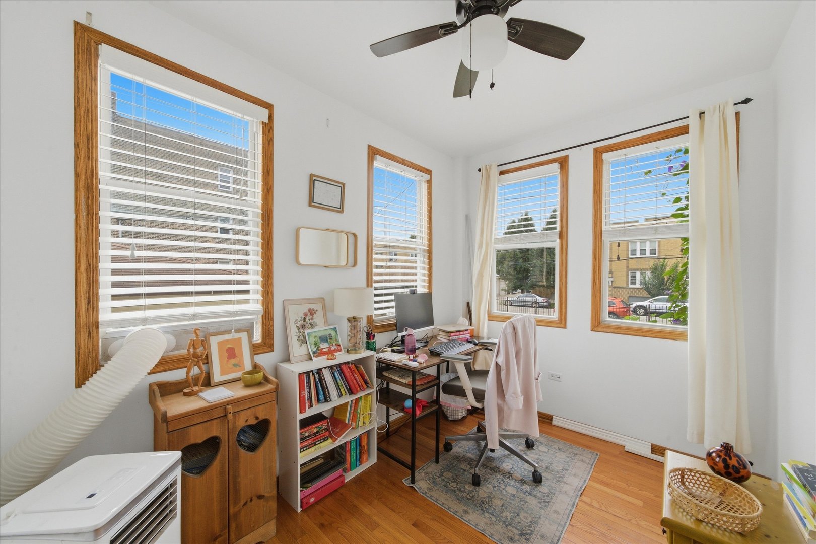 Home office with a computer desk, bookshelves, hardwood floors, and four wood-trimmed windows.