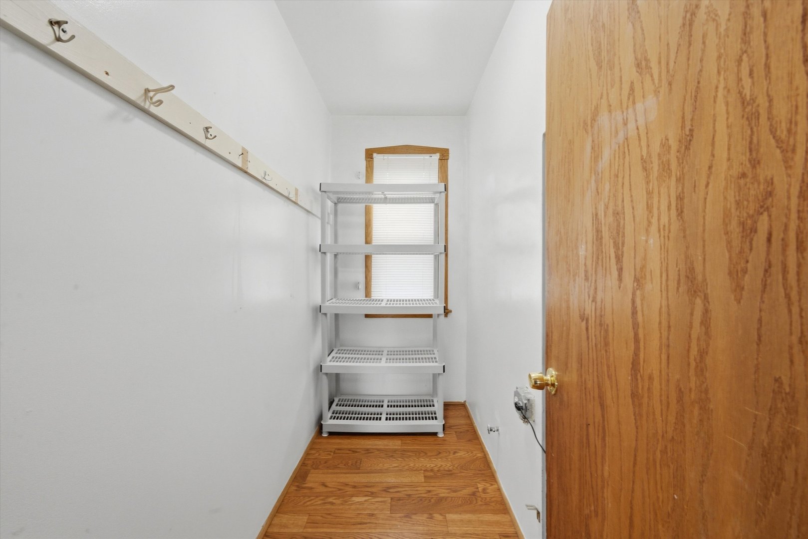 Narrow walk-in closet with hardwood flooring, wall hooks, and white wire shelving.