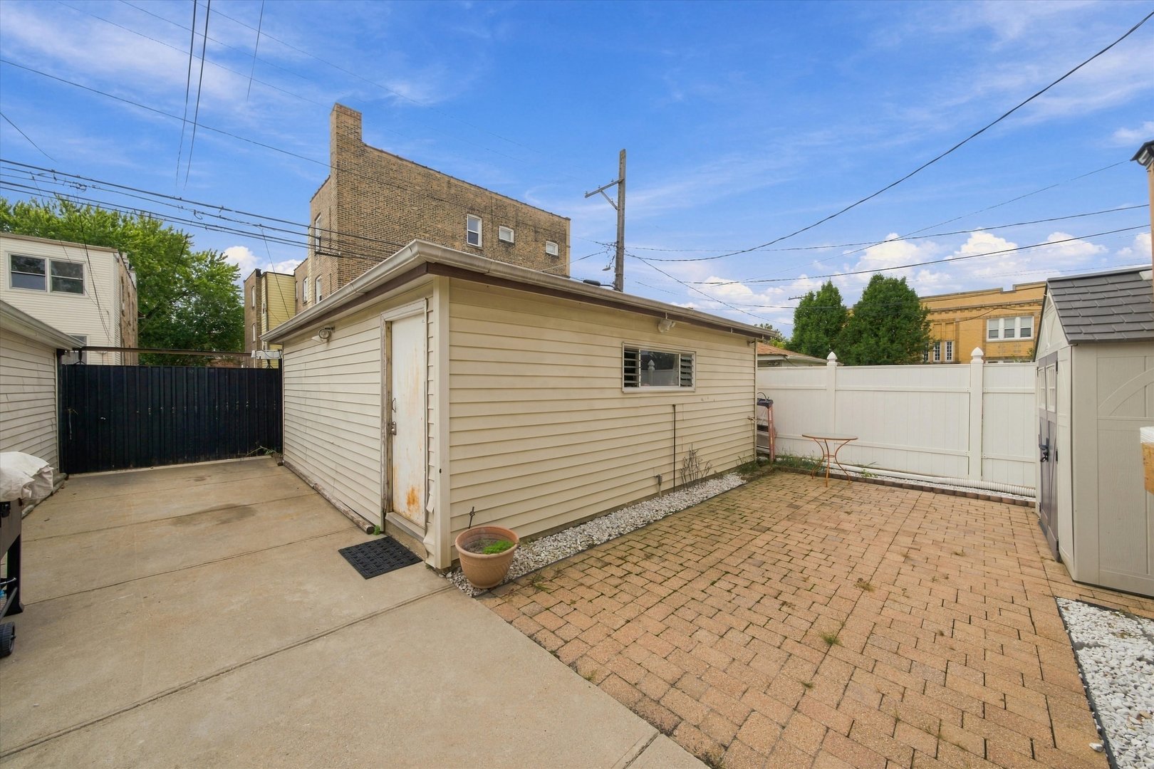Fenced backyard with a detached garage, concrete driveway, brick-paver patio, and small metal table.
