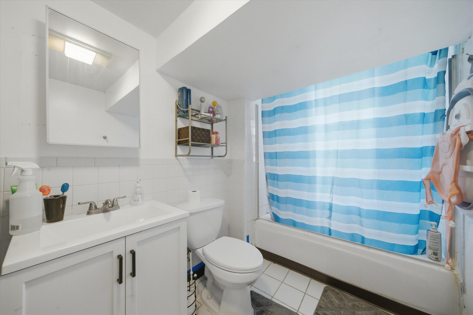 Bathroom with a white vanity, toilet, and tub behind a blue-and-white striped shower curtain.