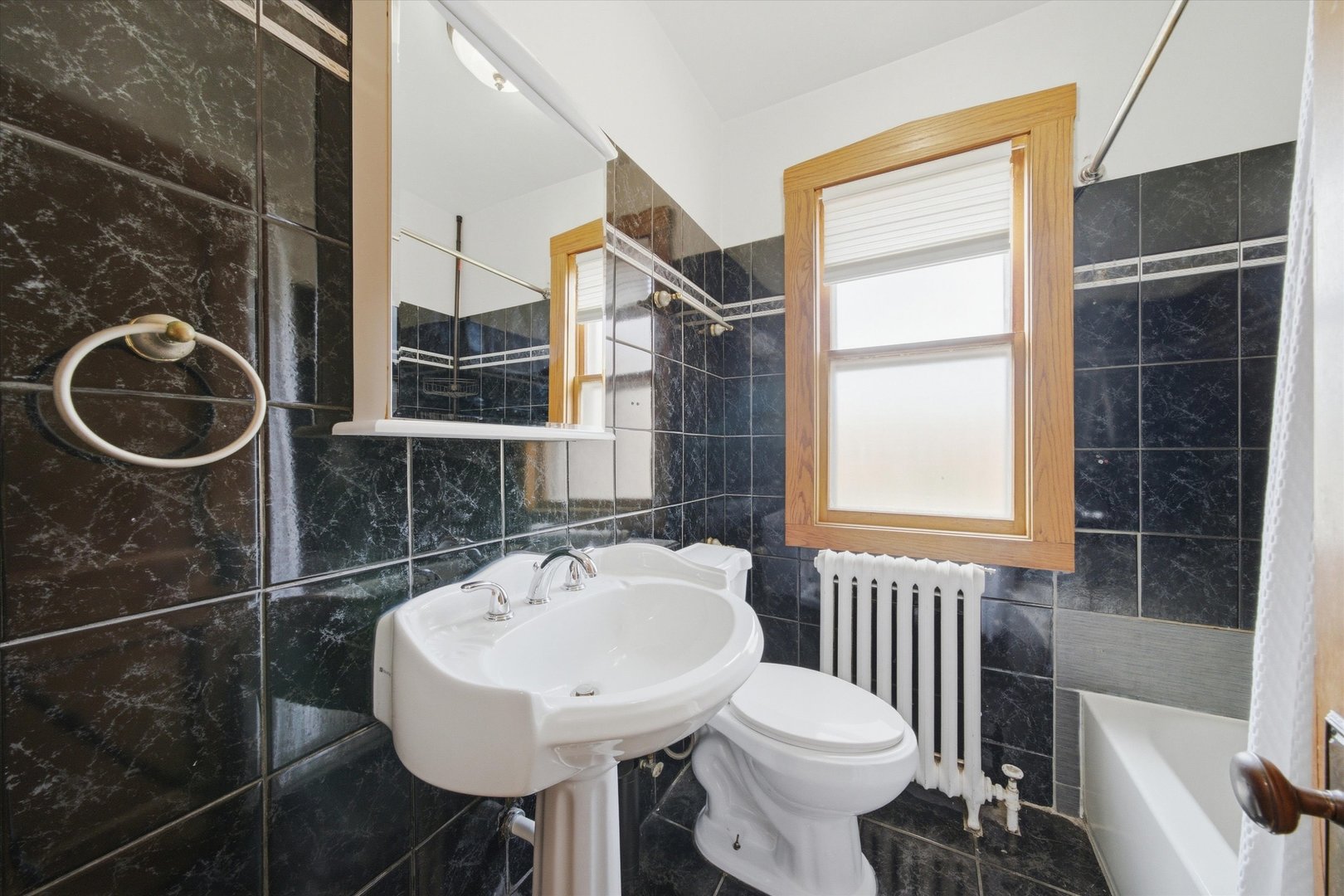 Bathroom with dark tile, pedestal sink, bathtub, and wood-trimmed window.