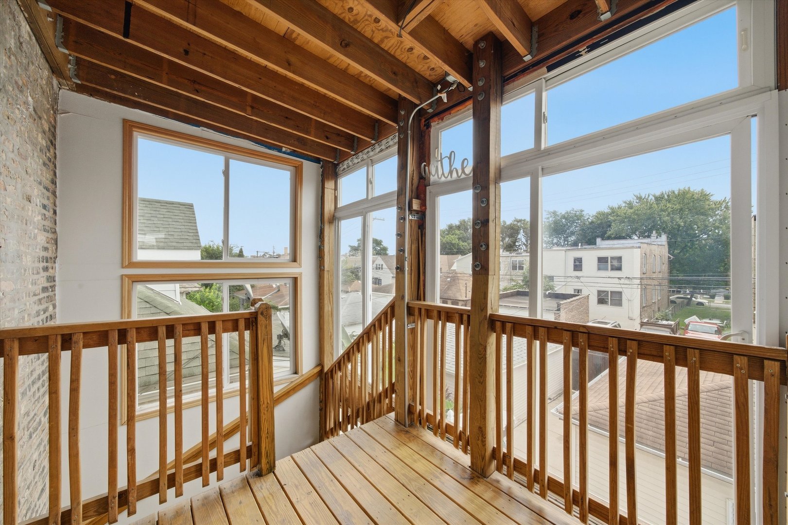 Enclosed porch with exposed wood beams, plank flooring, wooden railings, and large neighborhood-facing windows.
