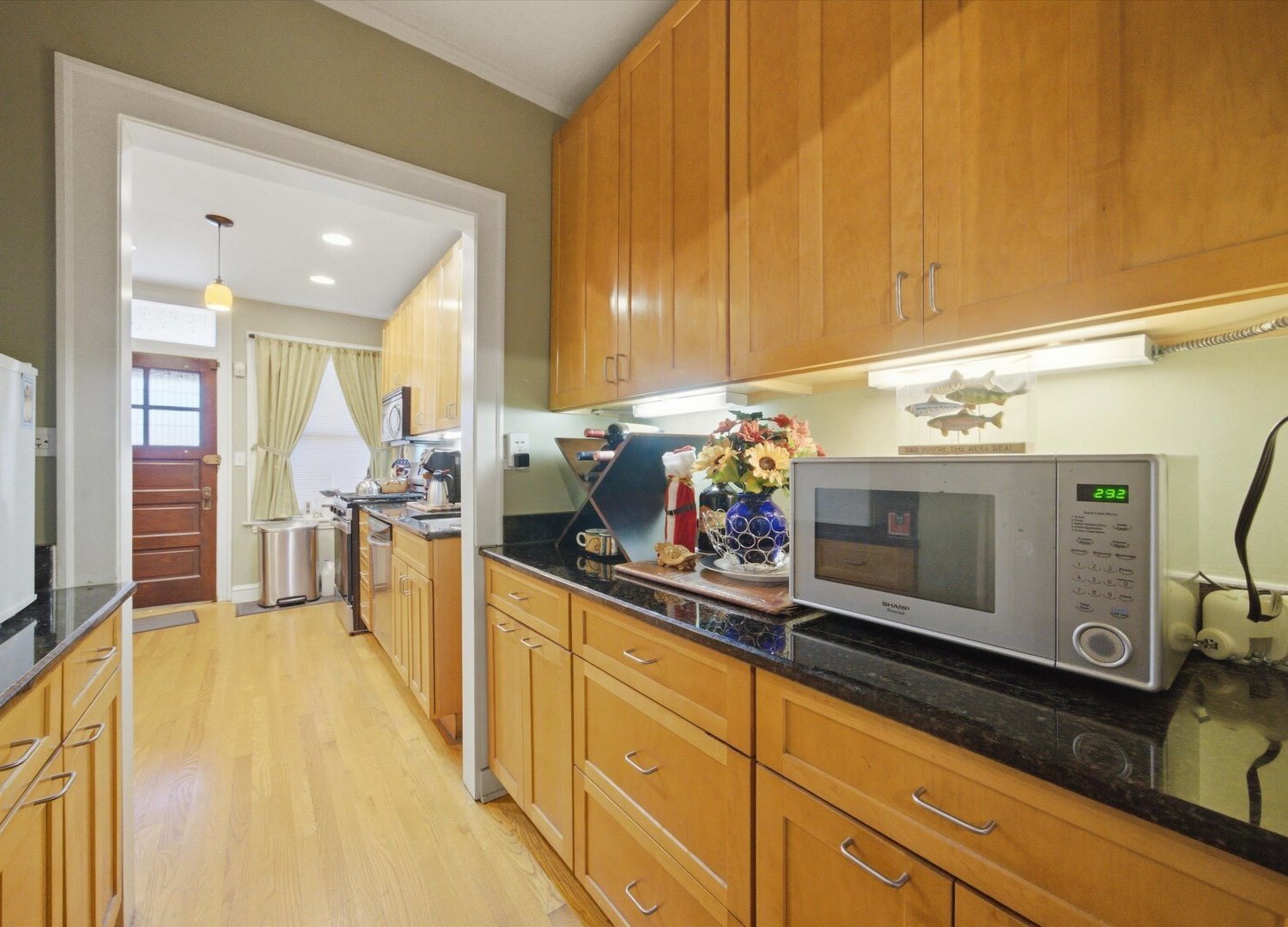 Kitchen with honey-colored cabinets, black countertops, and light hardwood floors.