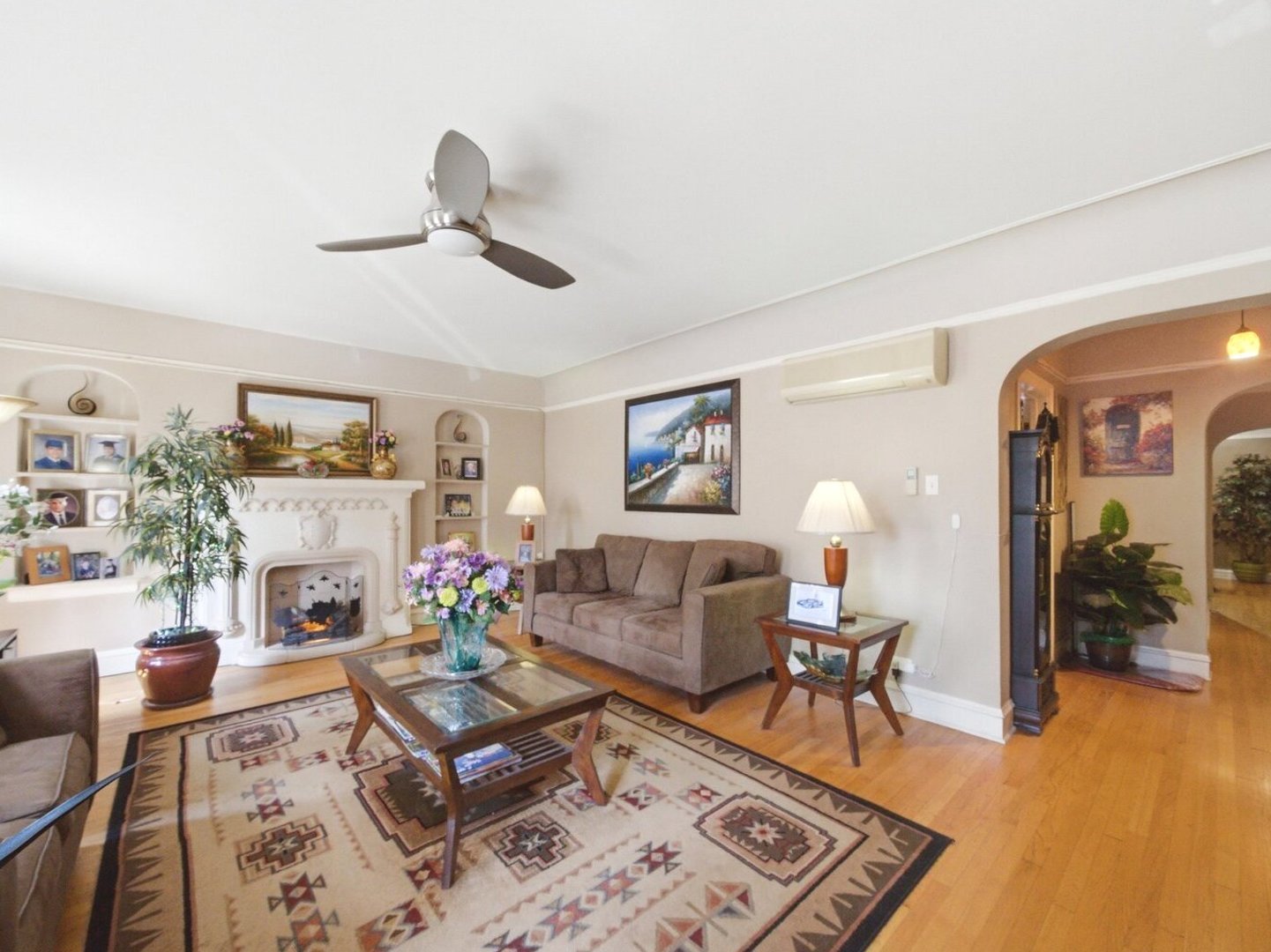 Living room with a decorative fireplace, brown sofa, patterned rug, and hardwood floors.