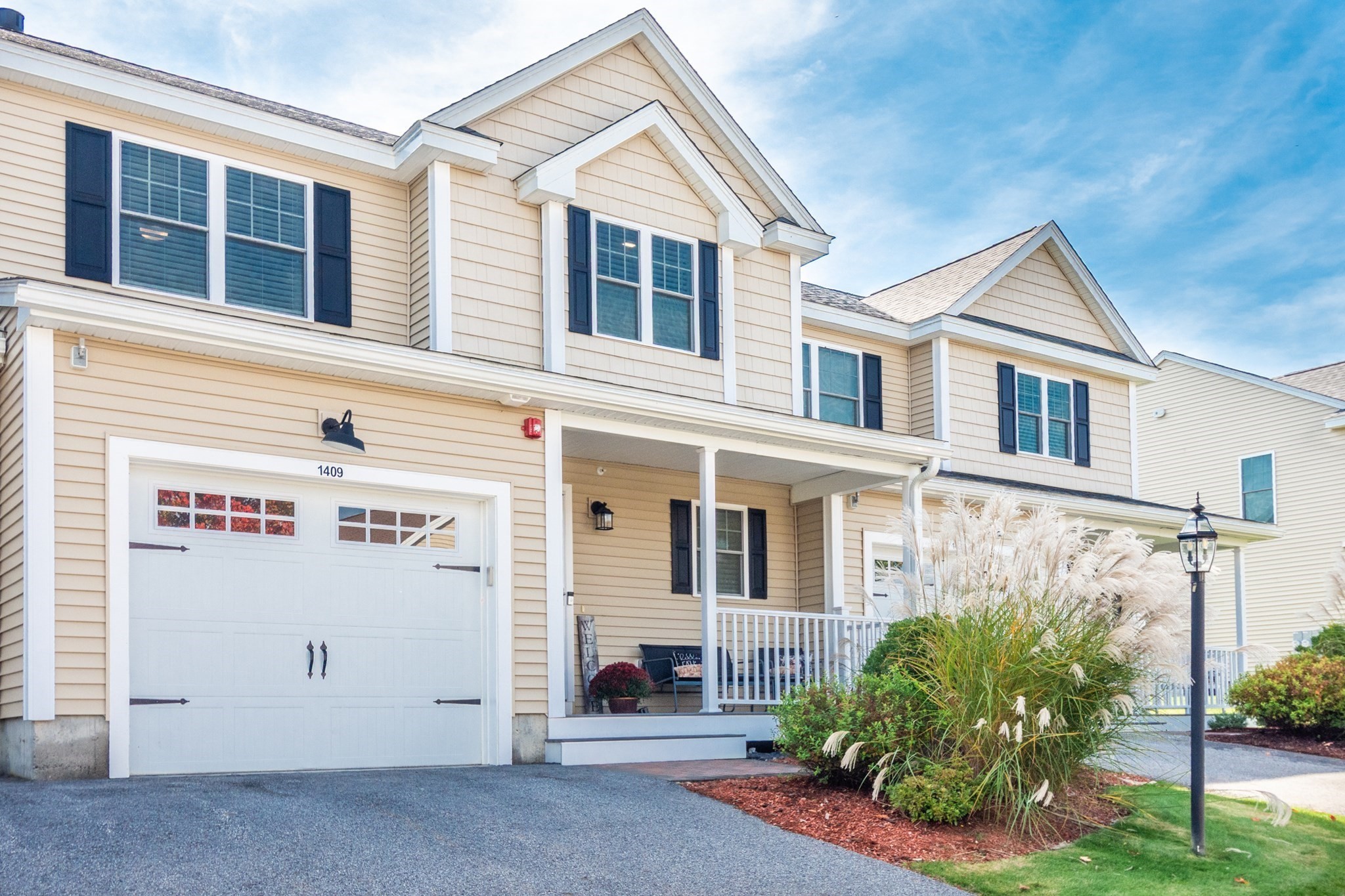 Beige two-story townhouse with attached garage marked 1409, covered porch, and ornamental grasses.
