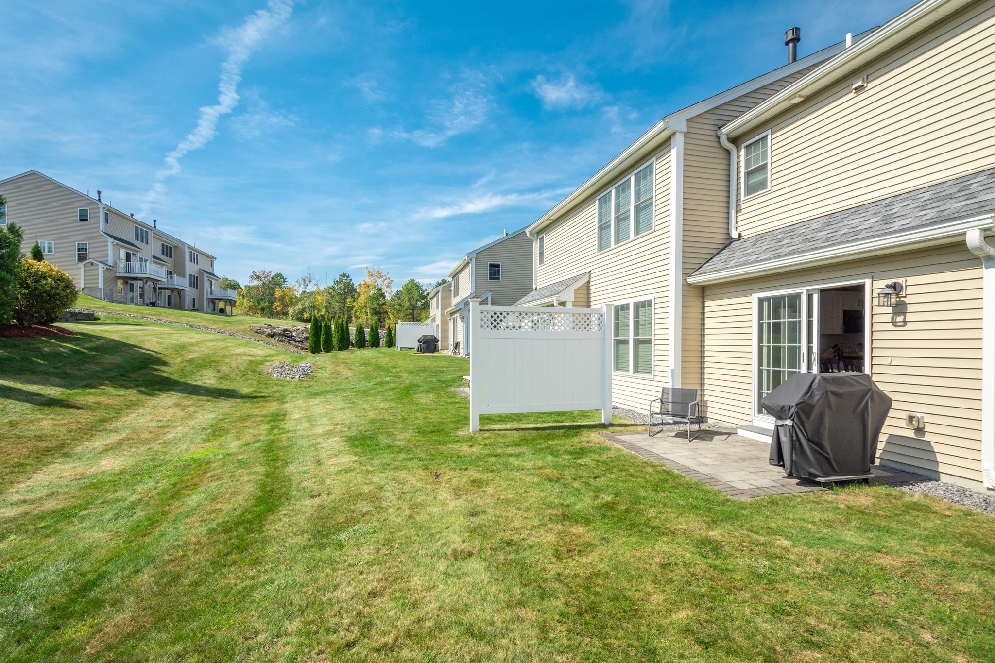 Townhouse rear patio with a covered grill and white privacy fence beside a sloping lawn.