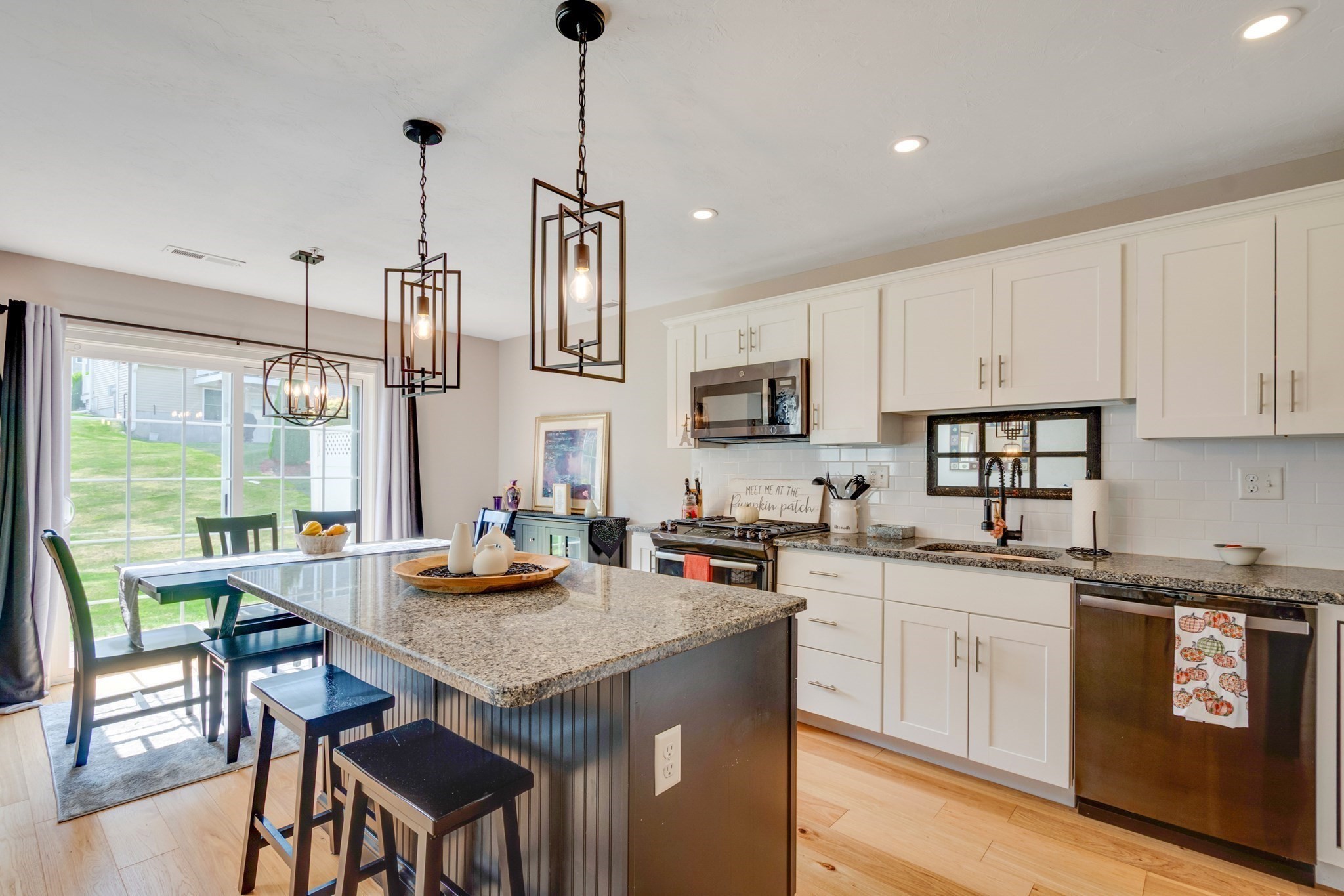 Kitchen with a large dark island, granite counters, white cabinets, and sliding doors to the lawn.
