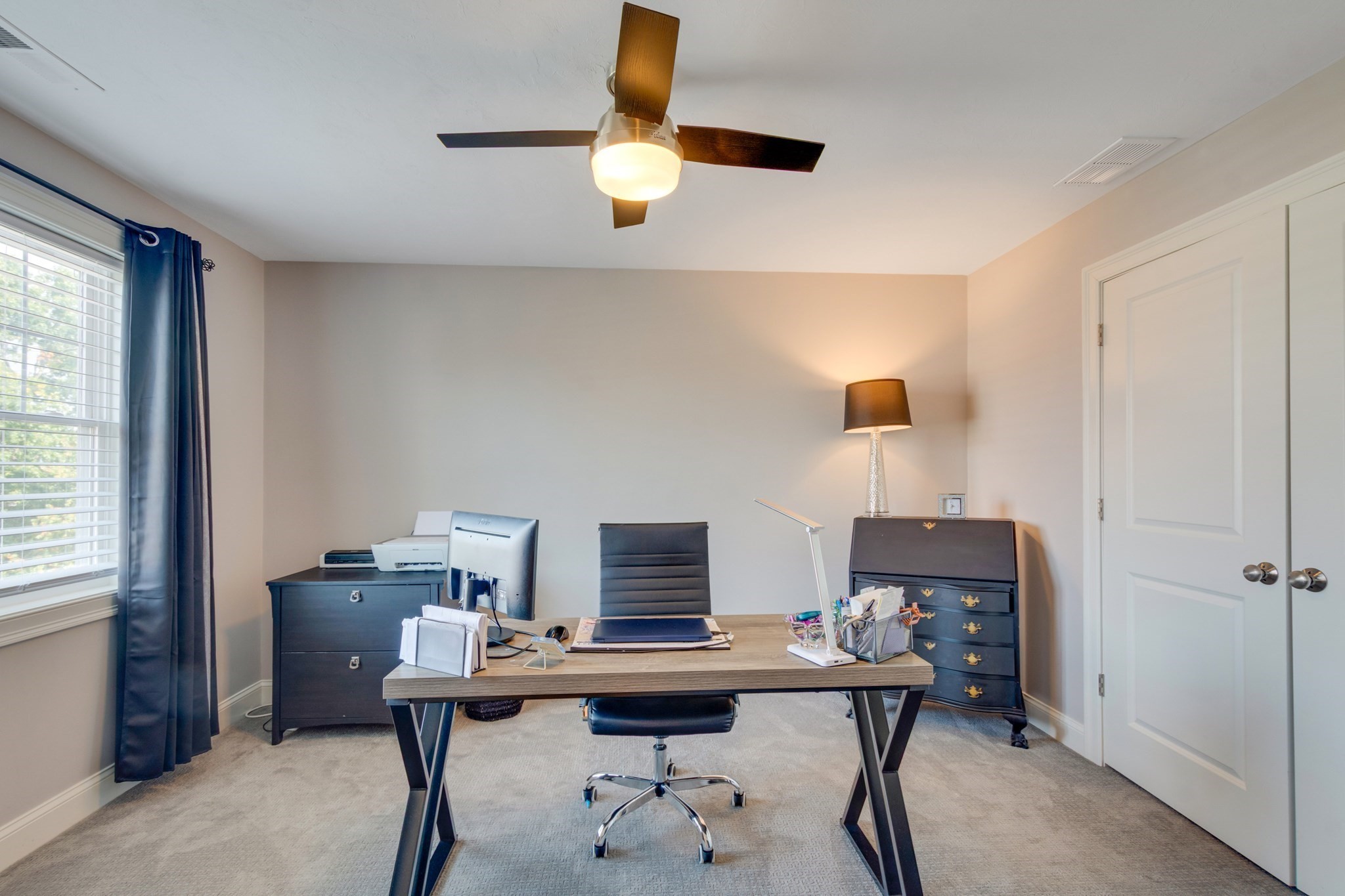 Furnished home office with a desk and computer, navy curtains, and a ceiling fan.