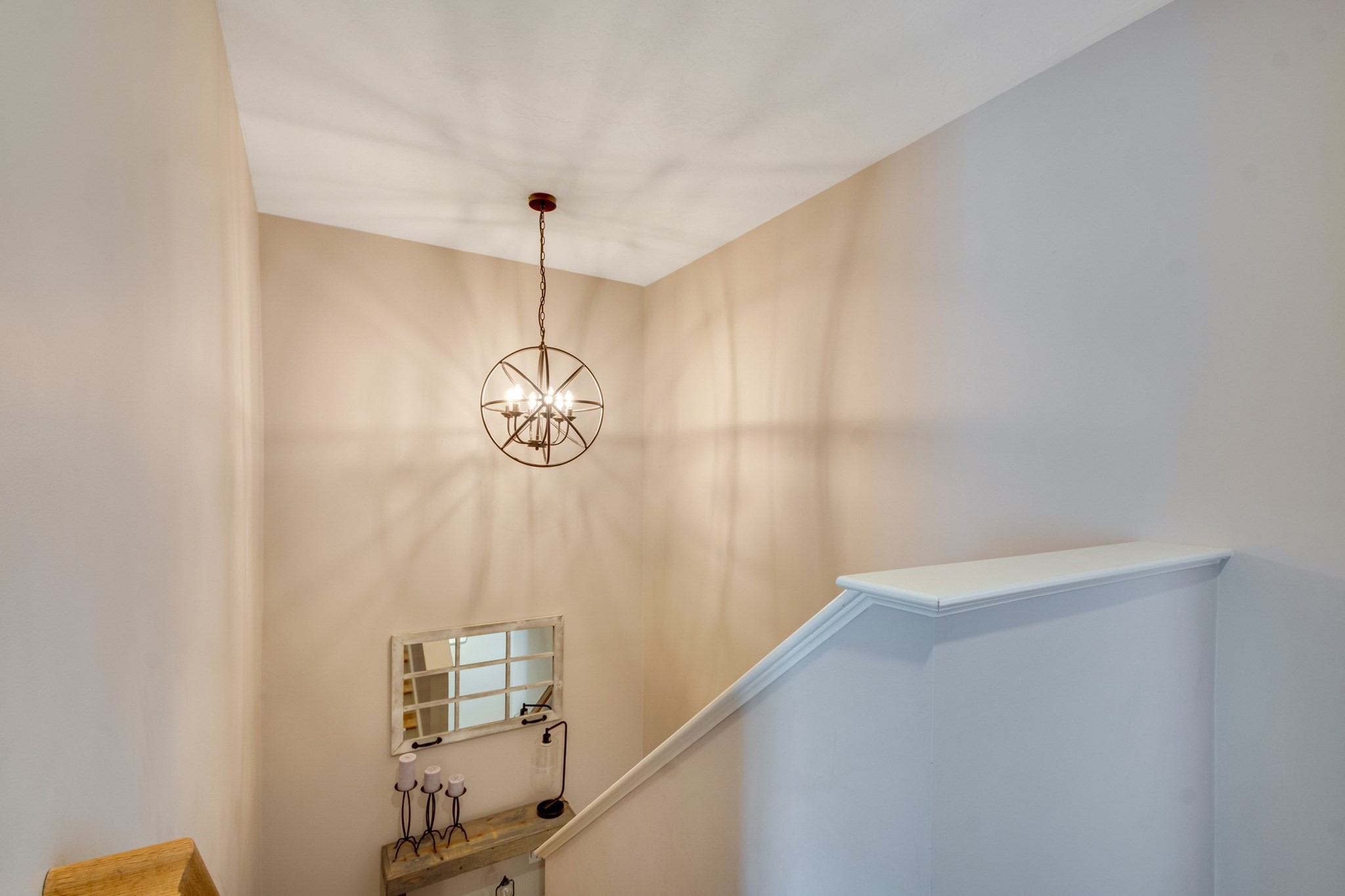 Staircase landing with a spherical metal chandelier, rustic console shelf, candles, and decorative mirror.
