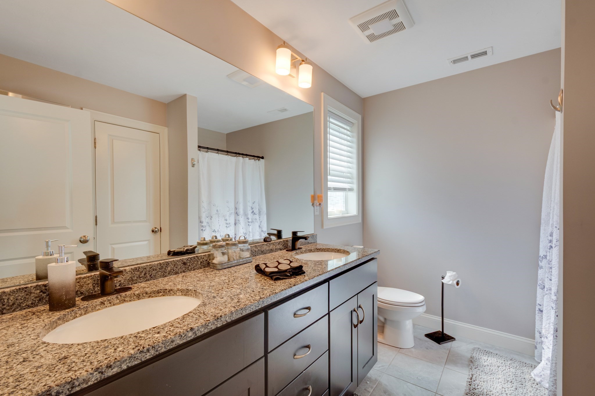 Bathroom with a granite double-sink vanity, dark cabinets, and tiled floor.
