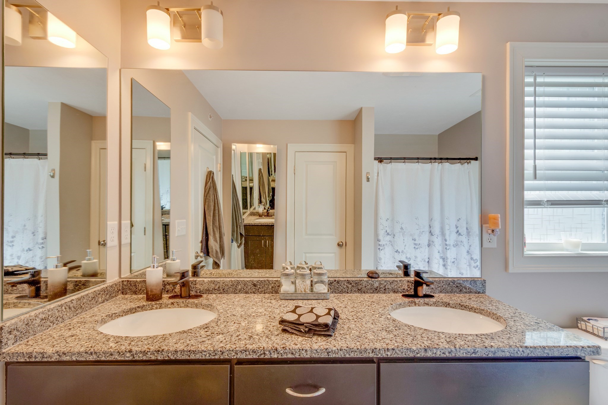 Bathroom with a granite double-sink vanity, mirrored wall, and curtained shower.
