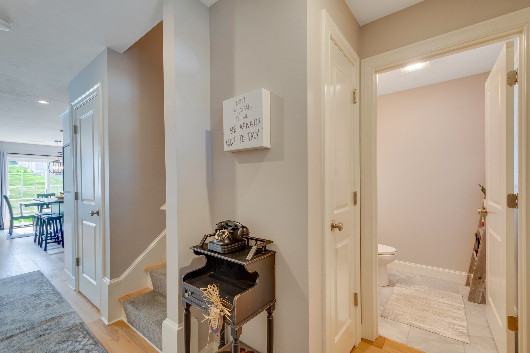Hallway with a vintage telephone on a console, staircase, dining area, and open bathroom door.