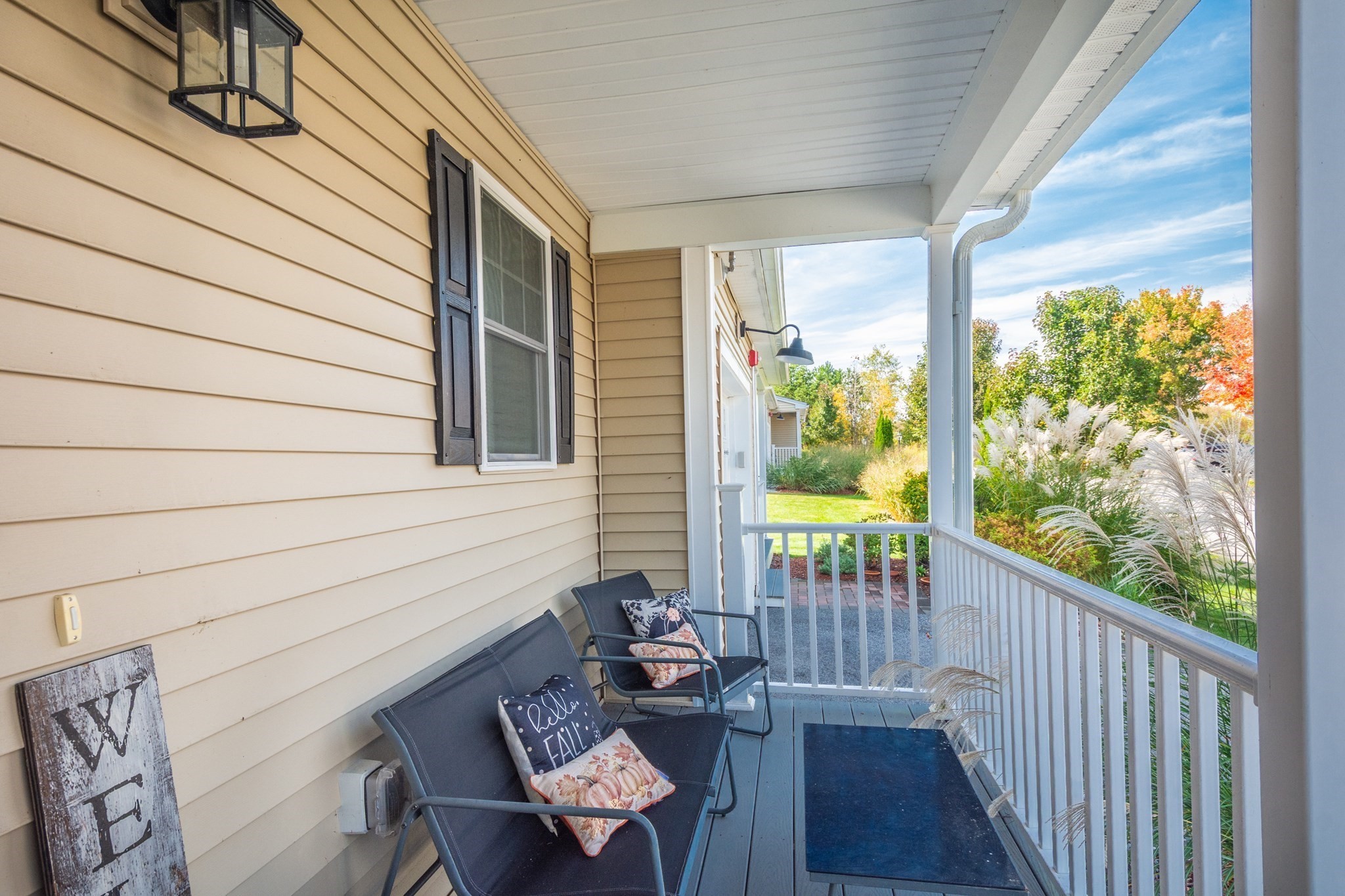 Covered front porch with cushioned chairs, white railing, and landscaped garden.