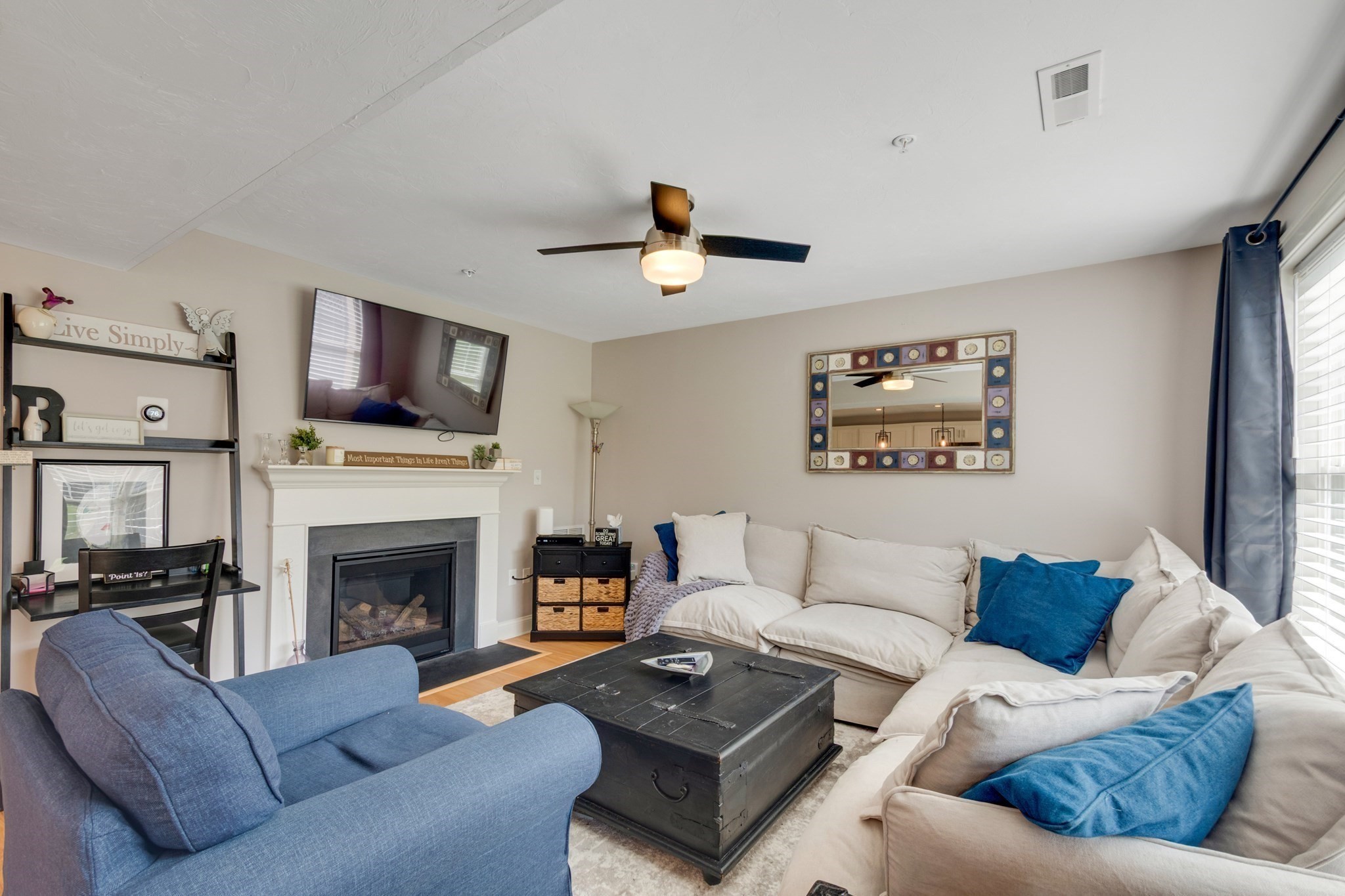 Living room with a white sectional, blue armchair, and fireplace beneath a wall-mounted television.