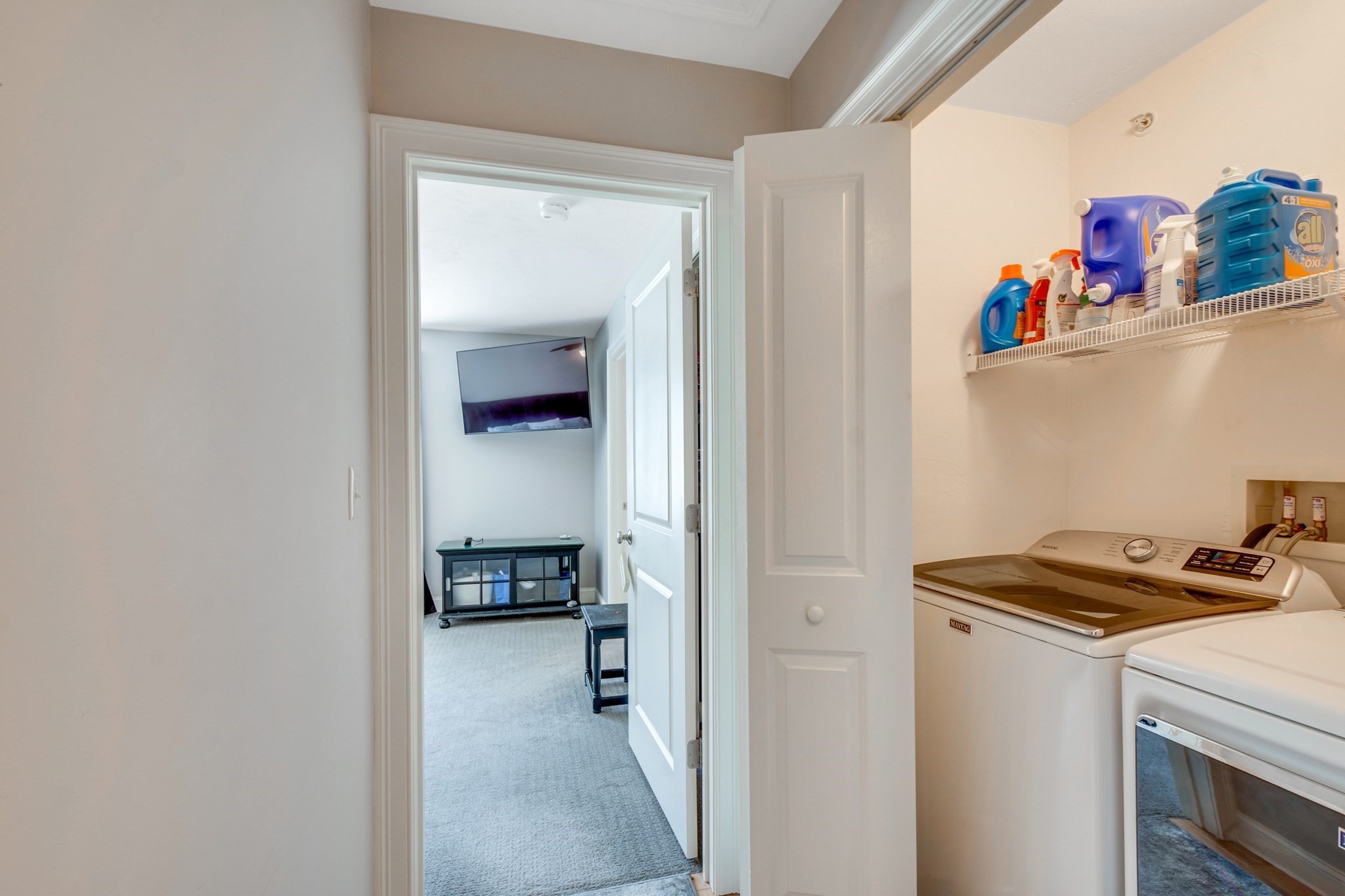 Laundry room with washer and dryer, detergent shelf, and doorway to a carpeted room.
