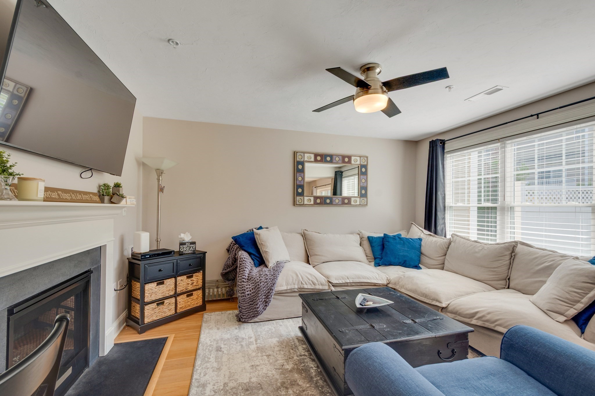 Living room with a white sectional, dark coffee table, fireplace, and large windows with blinds.