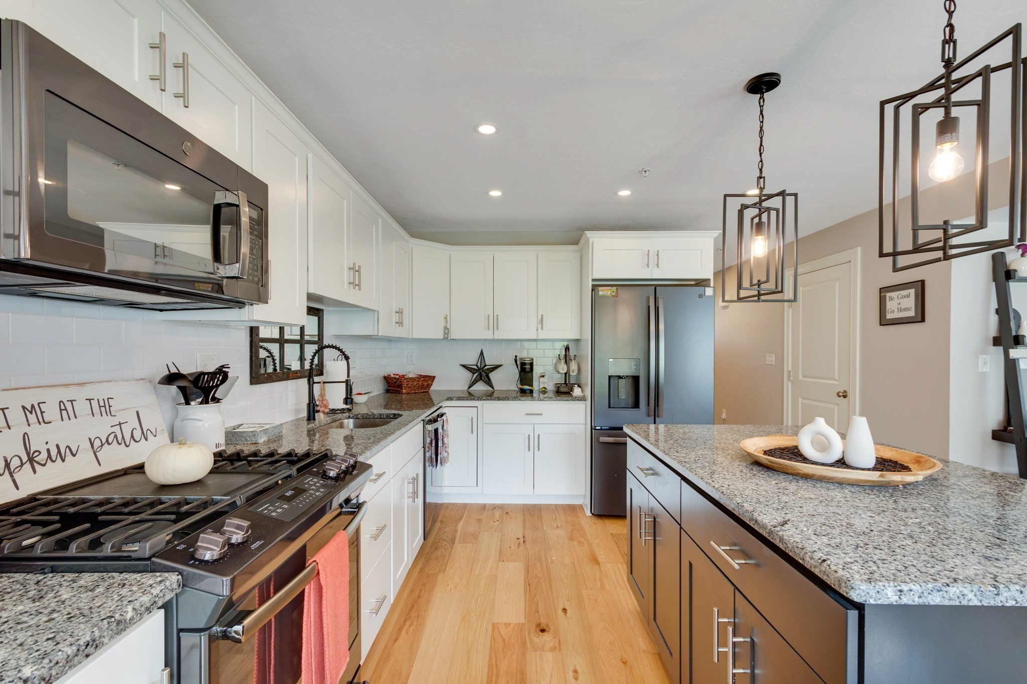 Kitchen with a granite island, white cabinetry, stainless steel appliances, and light wood floors.