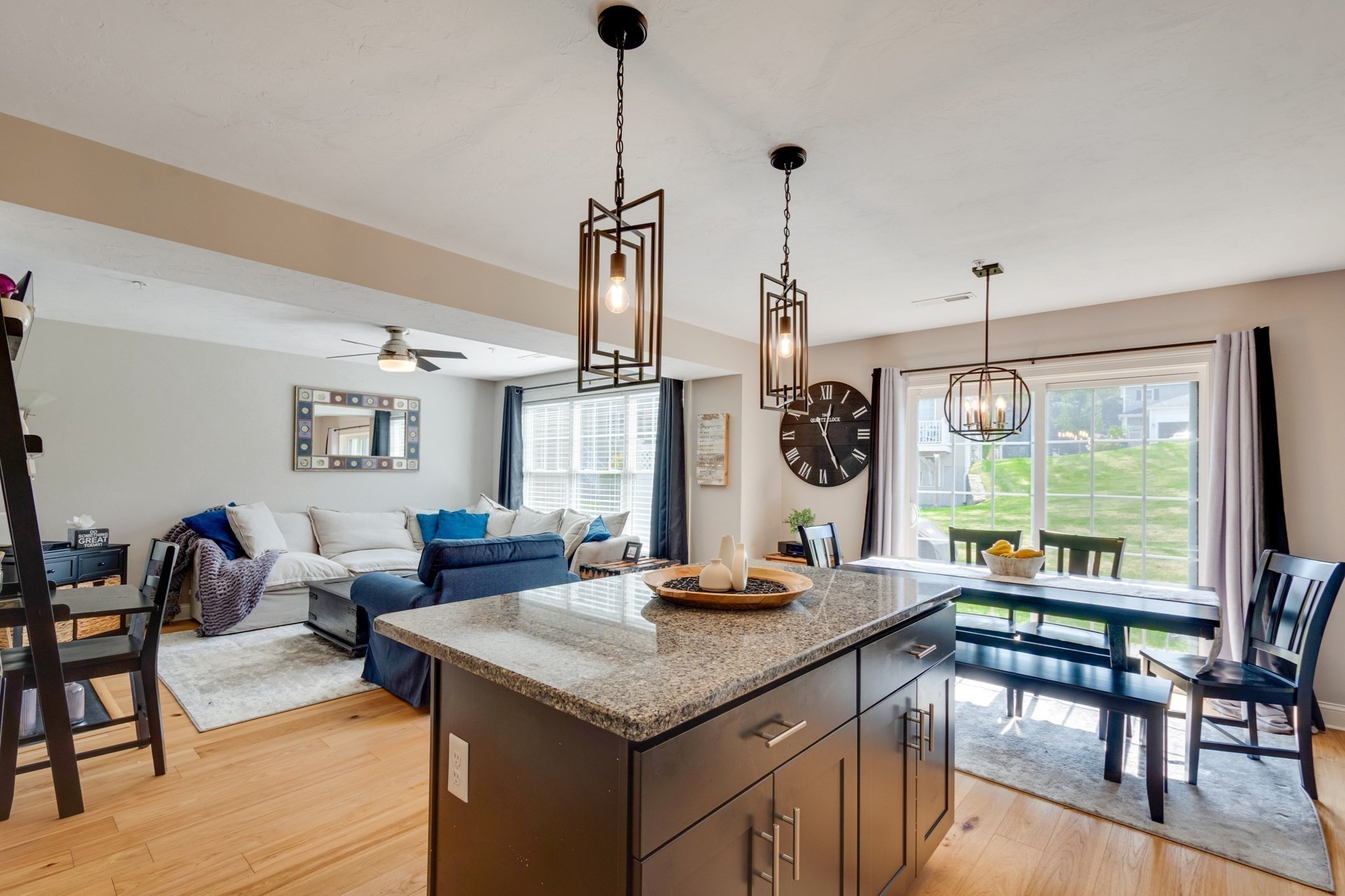 Open-plan kitchen and living room with a granite island, blue-and-white seating, and sliding glass doors.