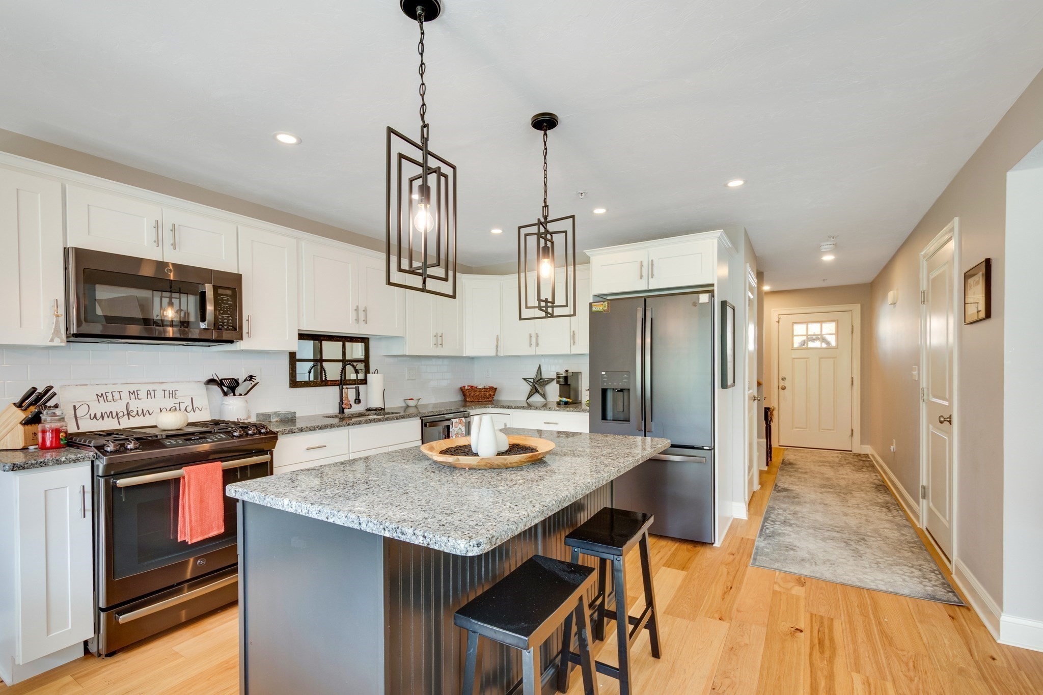 Kitchen with white cabinets, stainless appliances, and a granite island with bar stools.