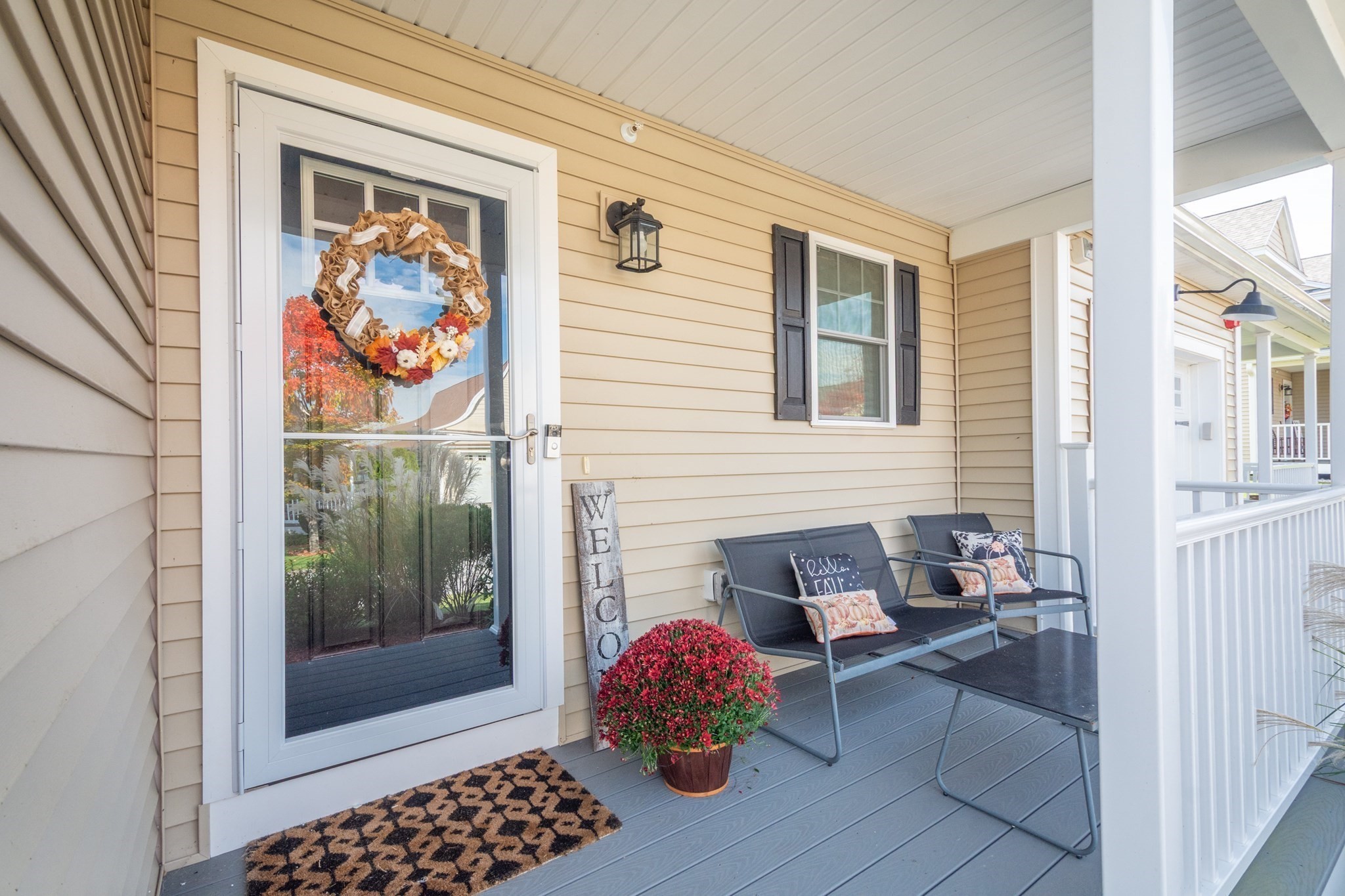 Covered porch with autumn wreath on the glass door, gray deck, and outdoor seating.