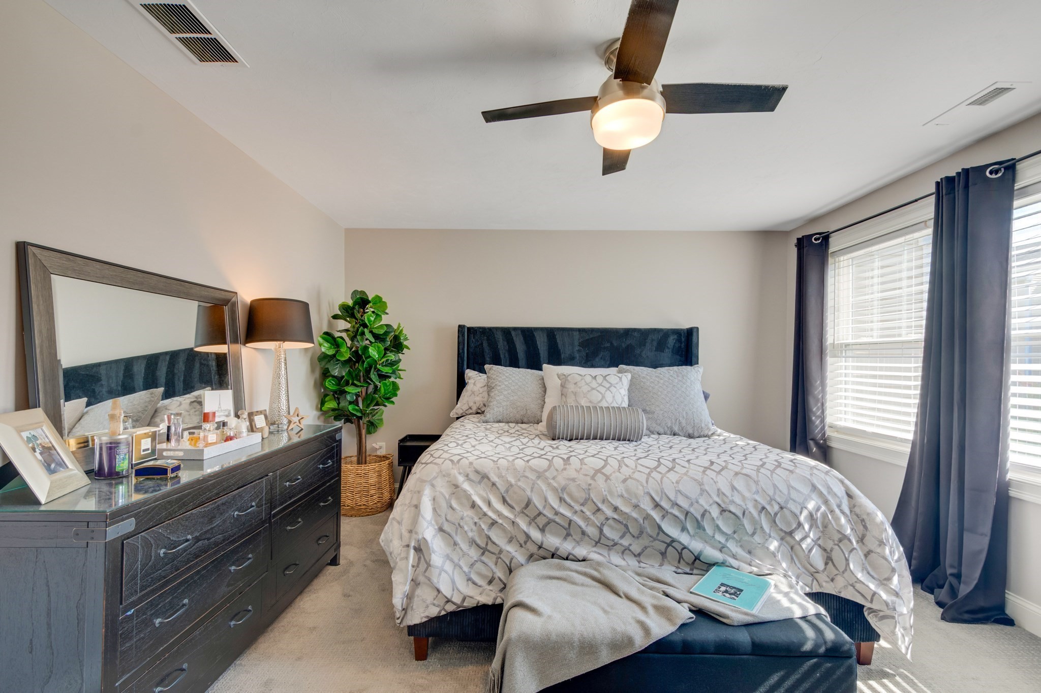 Bedroom with a large patterned bed, navy headboard, and dark curtains beside a bright window.