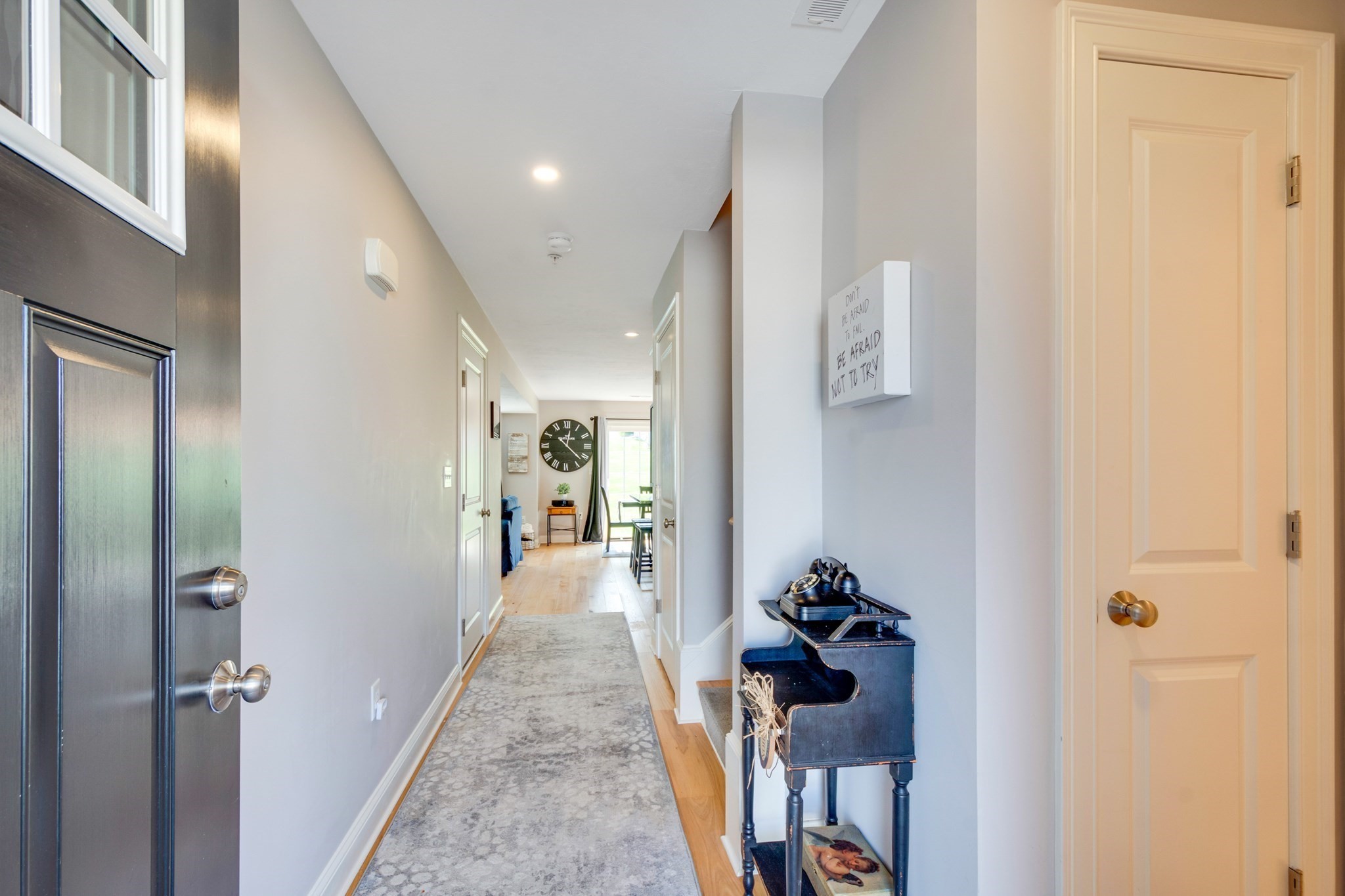 Furnished entry hallway with a patterned runner, dark front door, and view toward the living area.