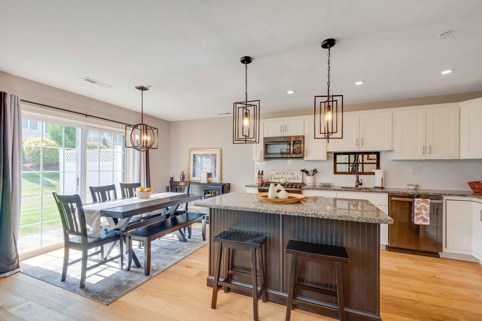 Kitchen and dining area with a dark island, granite counters, white cabinets, and a sunlit sliding glass door.