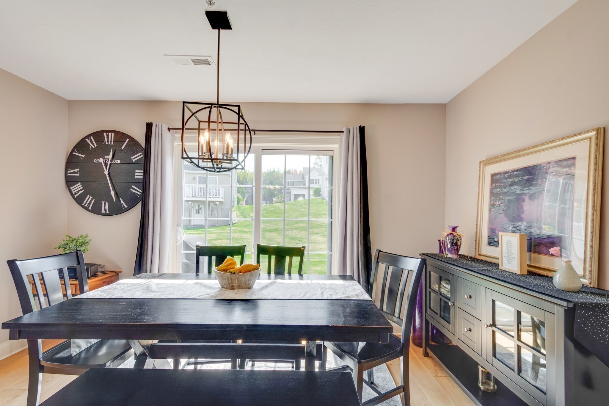 Dining room with a dark table, oversized Roman numeral clock, and sliding doors overlooking a lawn.