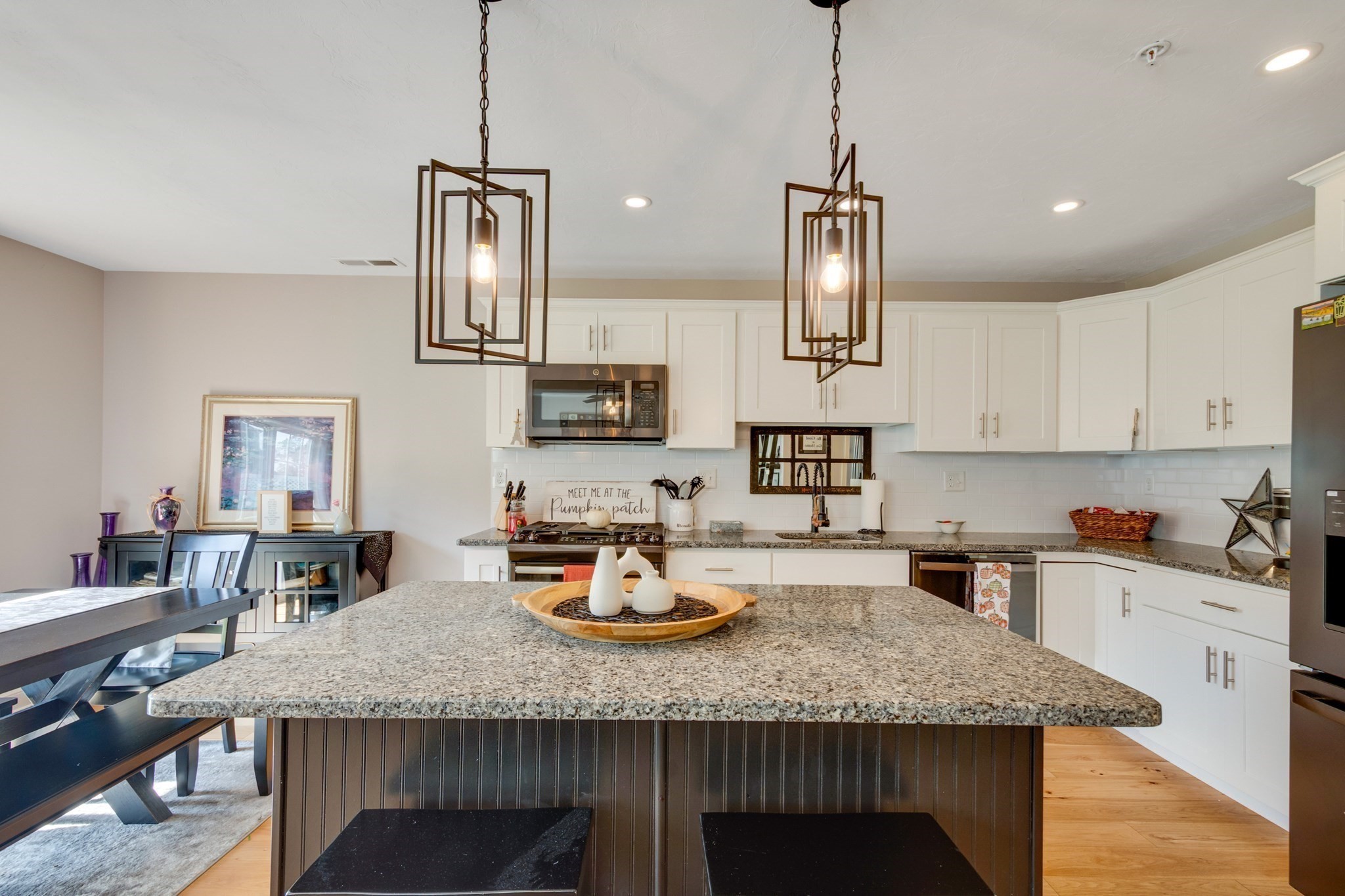 Kitchen with a large granite island, white cabinetry, geometric pendant lights, and an adjoining dining area.