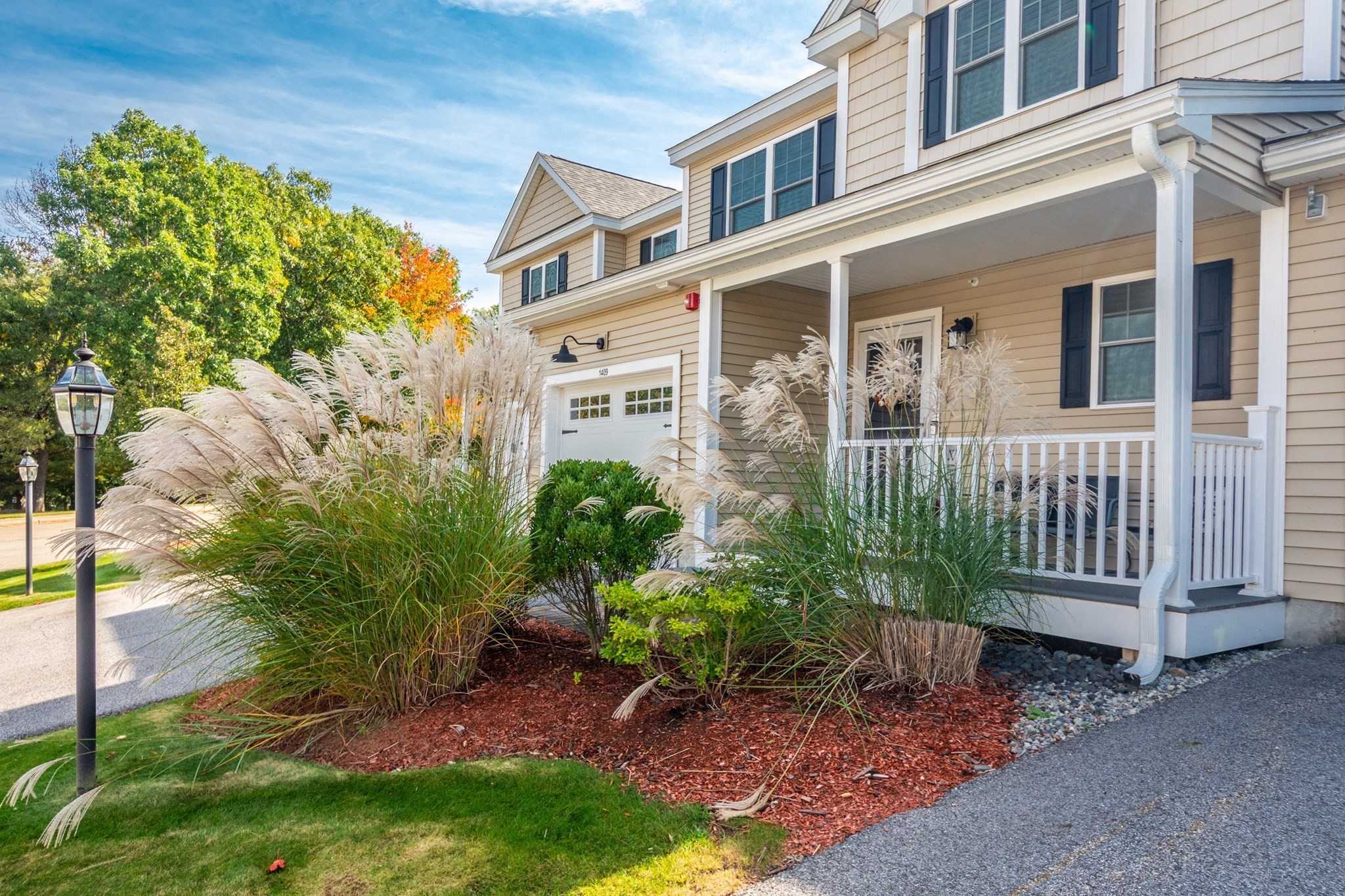 Beige home with a covered porch, attached garage, and landscaped garden of ornamental grasses.