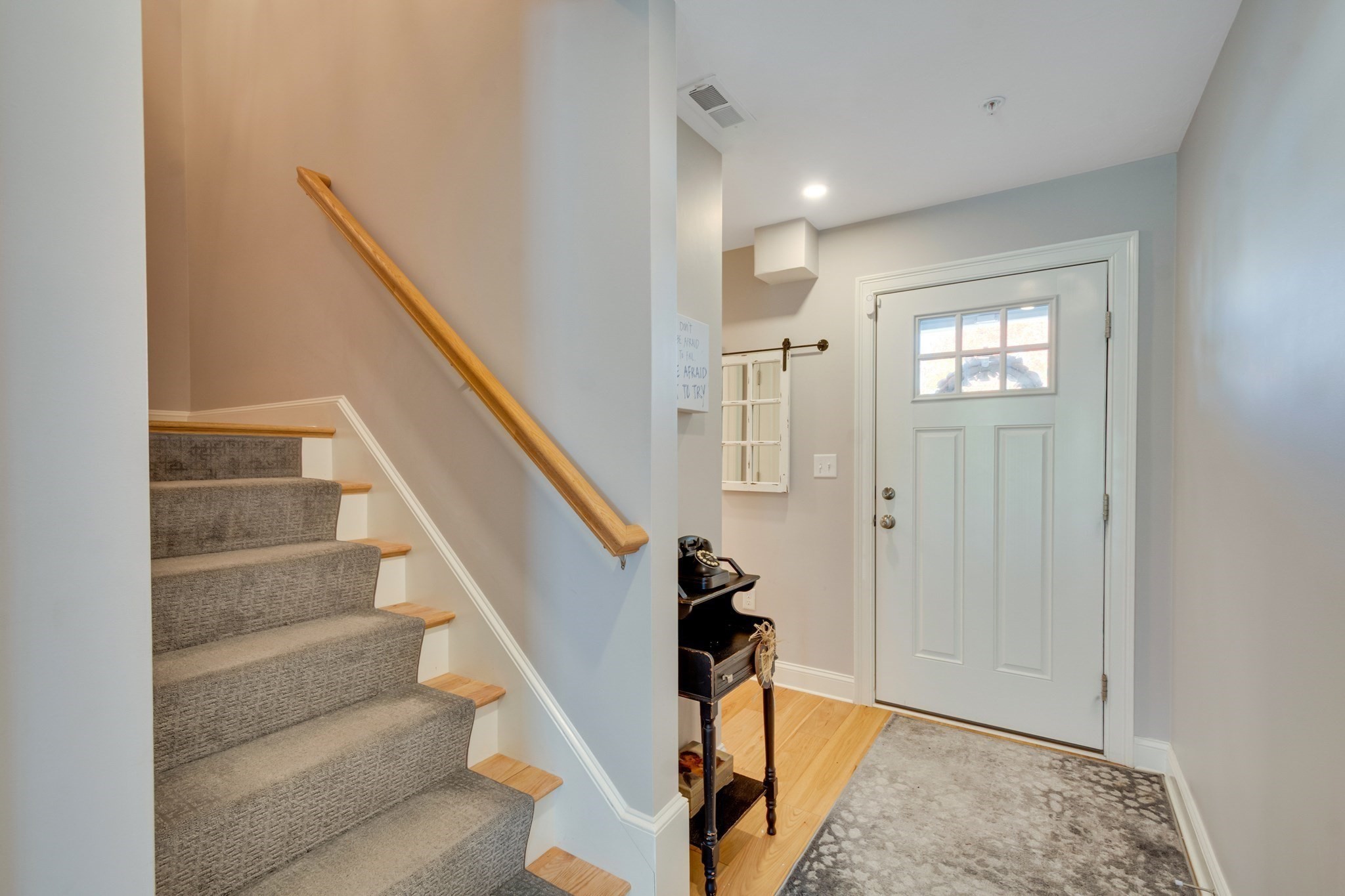 Entryway with a carpeted staircase beside a white front door and patterned rug.