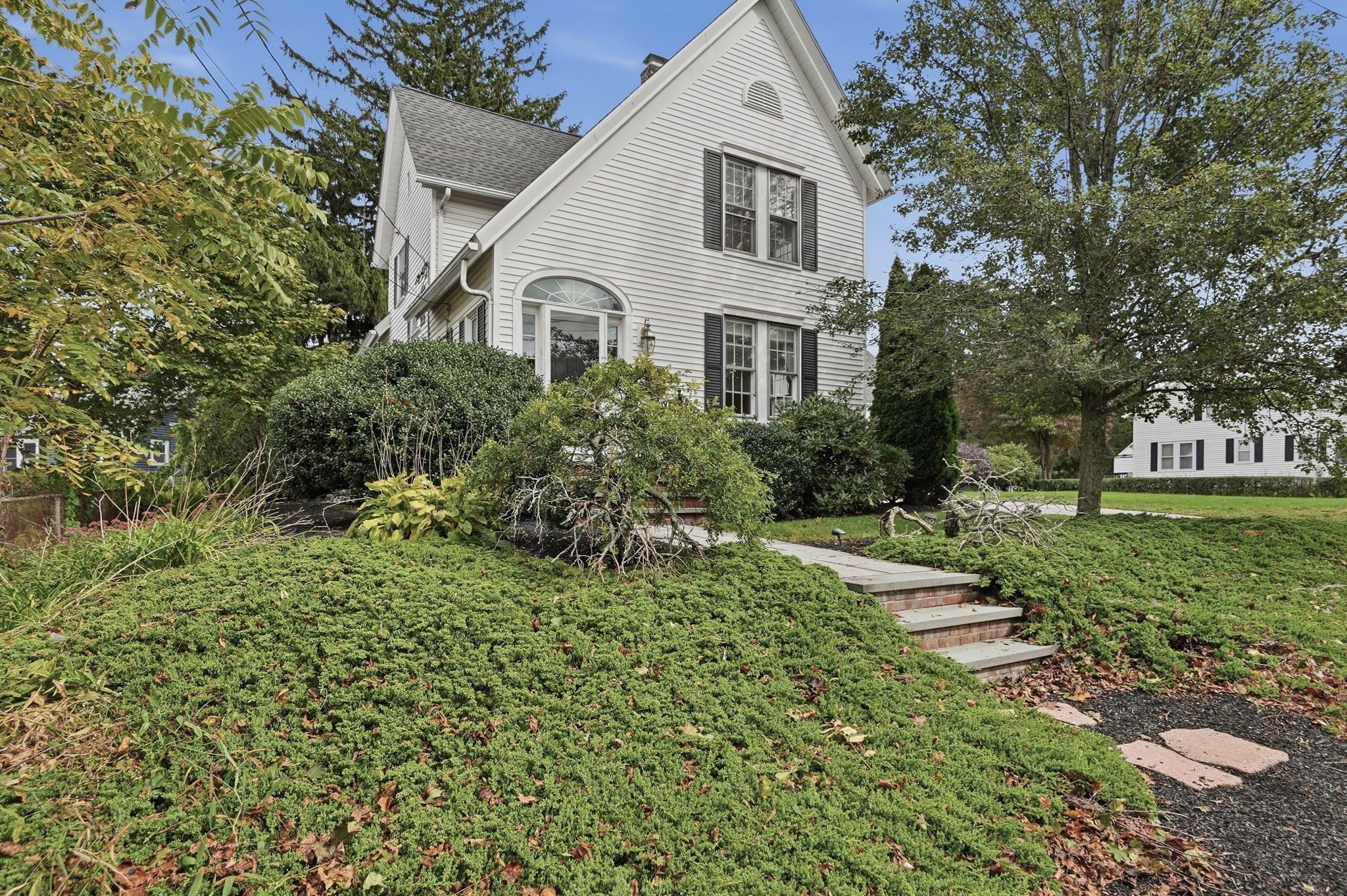 White gabled house with black shutters, an arched entry window, and landscaped front yard.