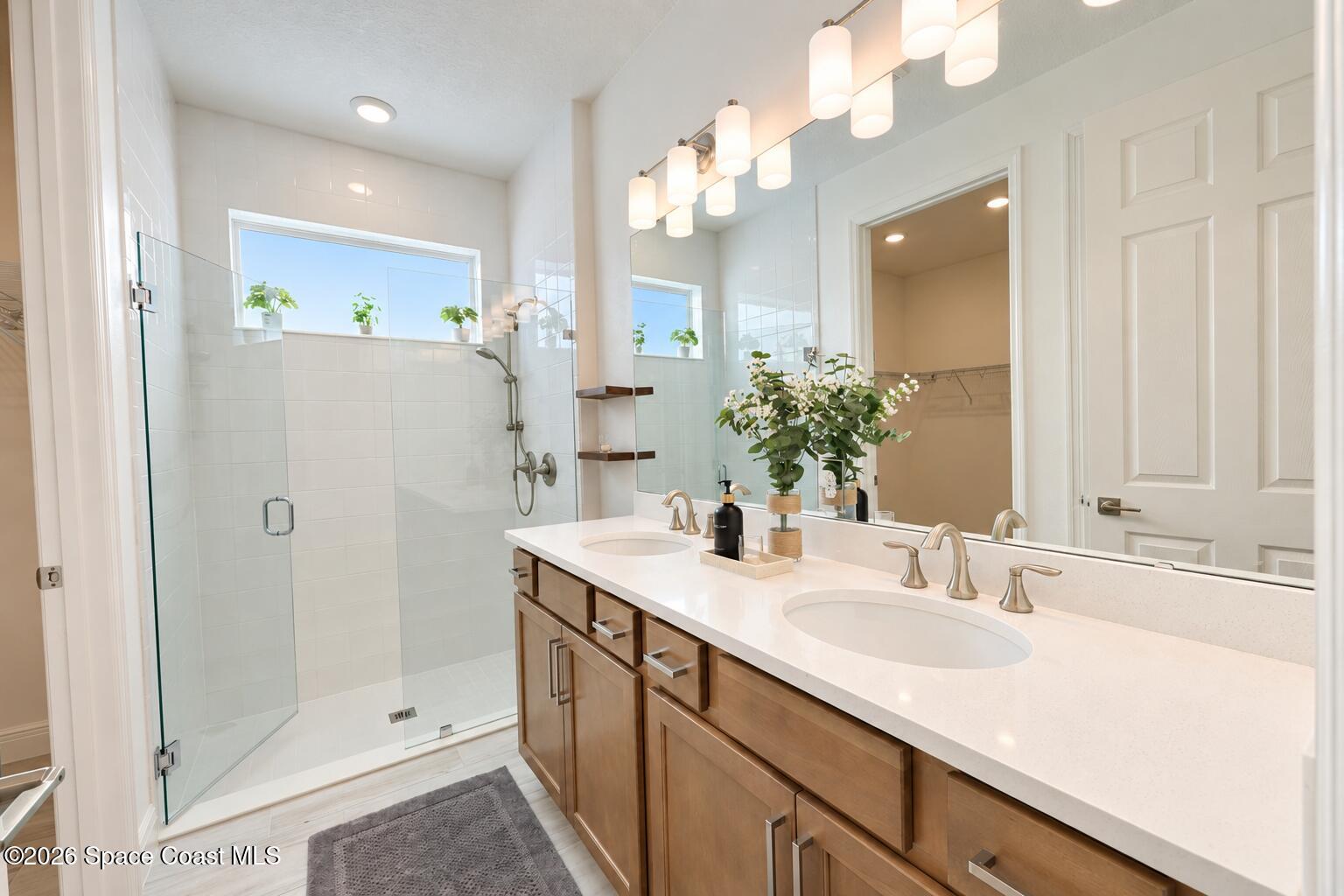 Bathroom with double-sink wood vanity, large mirror, and glass-enclosed walk-in shower.