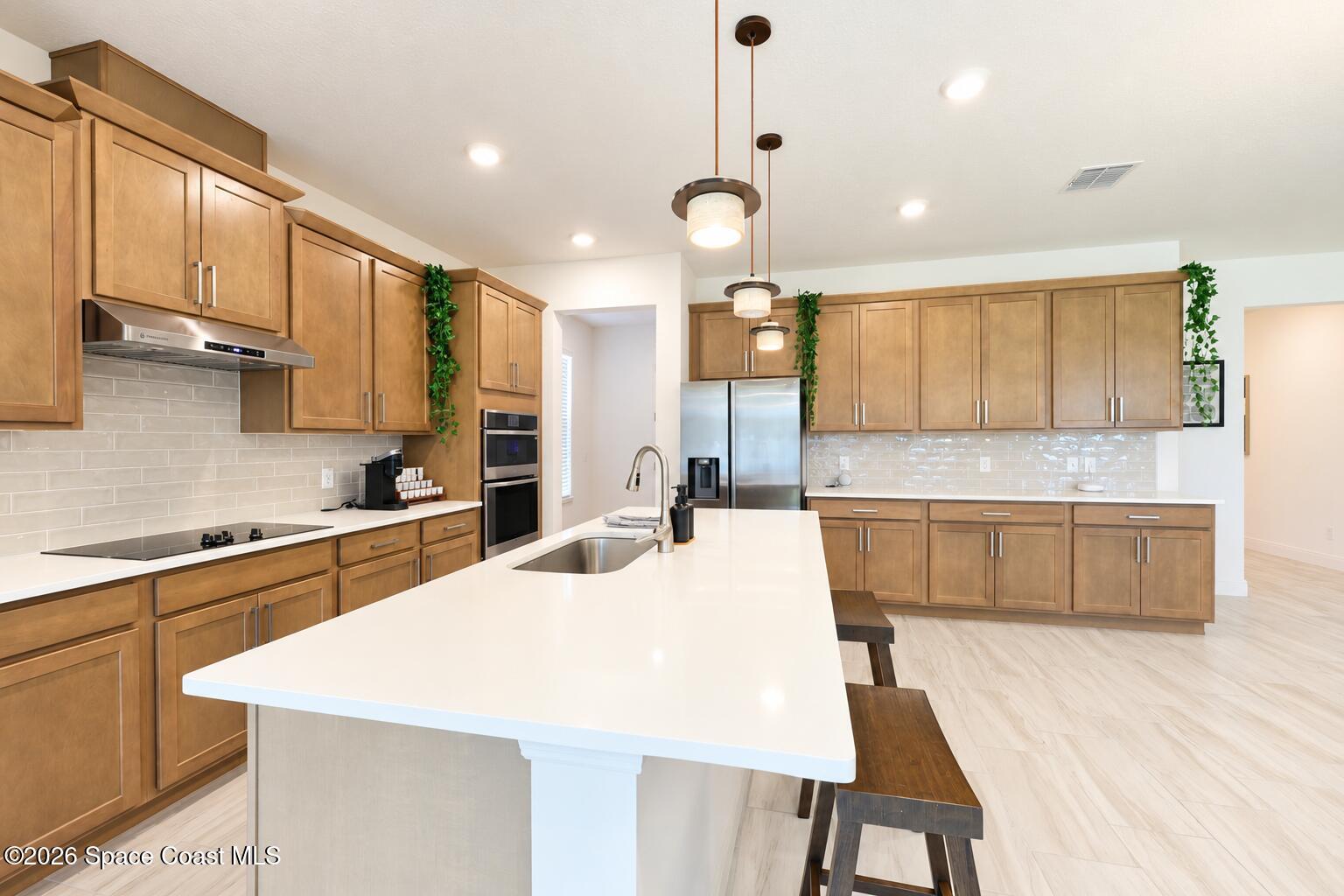 Kitchen with warm wood cabinets, stainless appliances, and a large white island with sink.