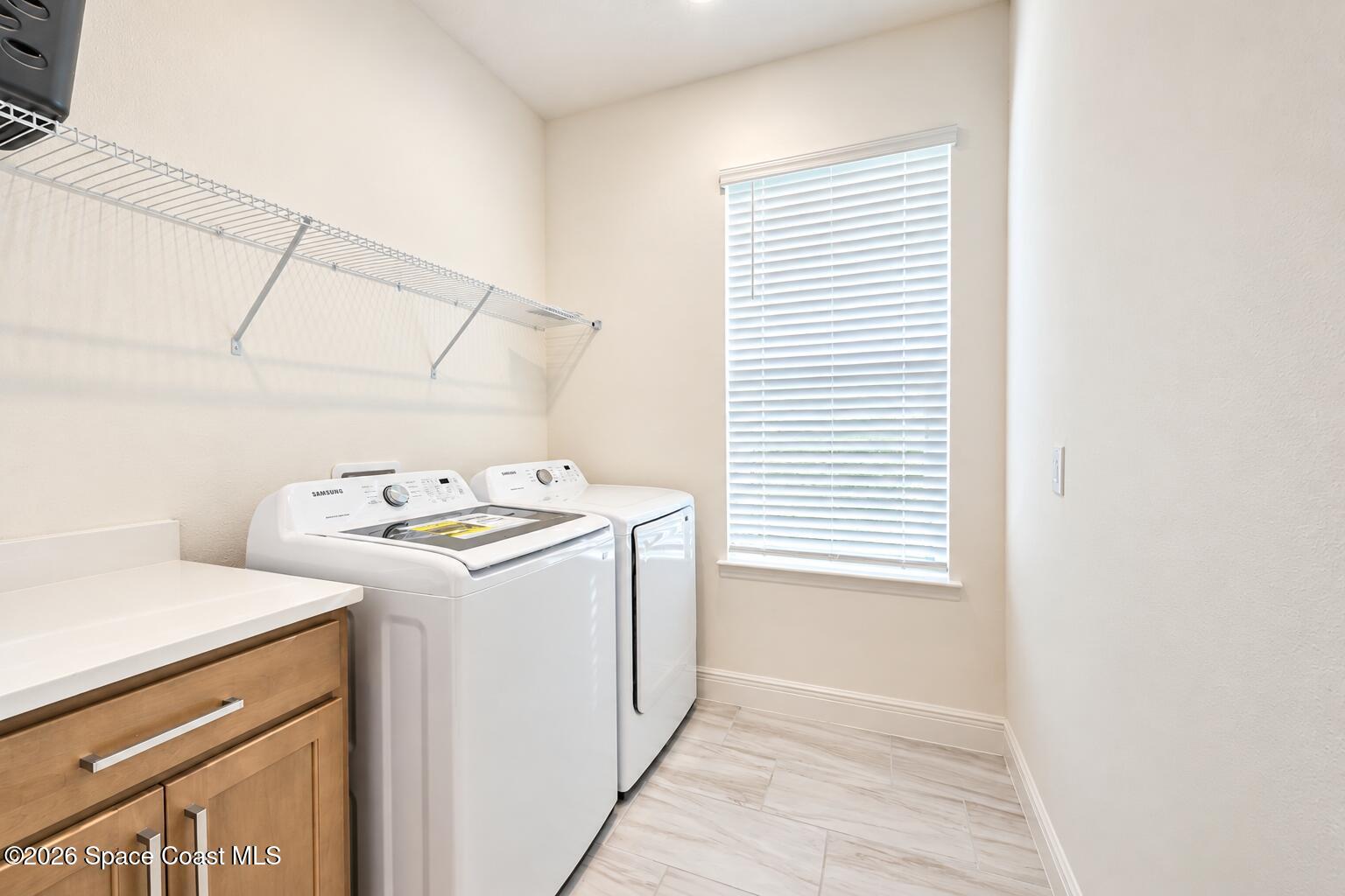 Laundry room with white washer and dryer, wire shelving, wood vanity, and a window with blinds.