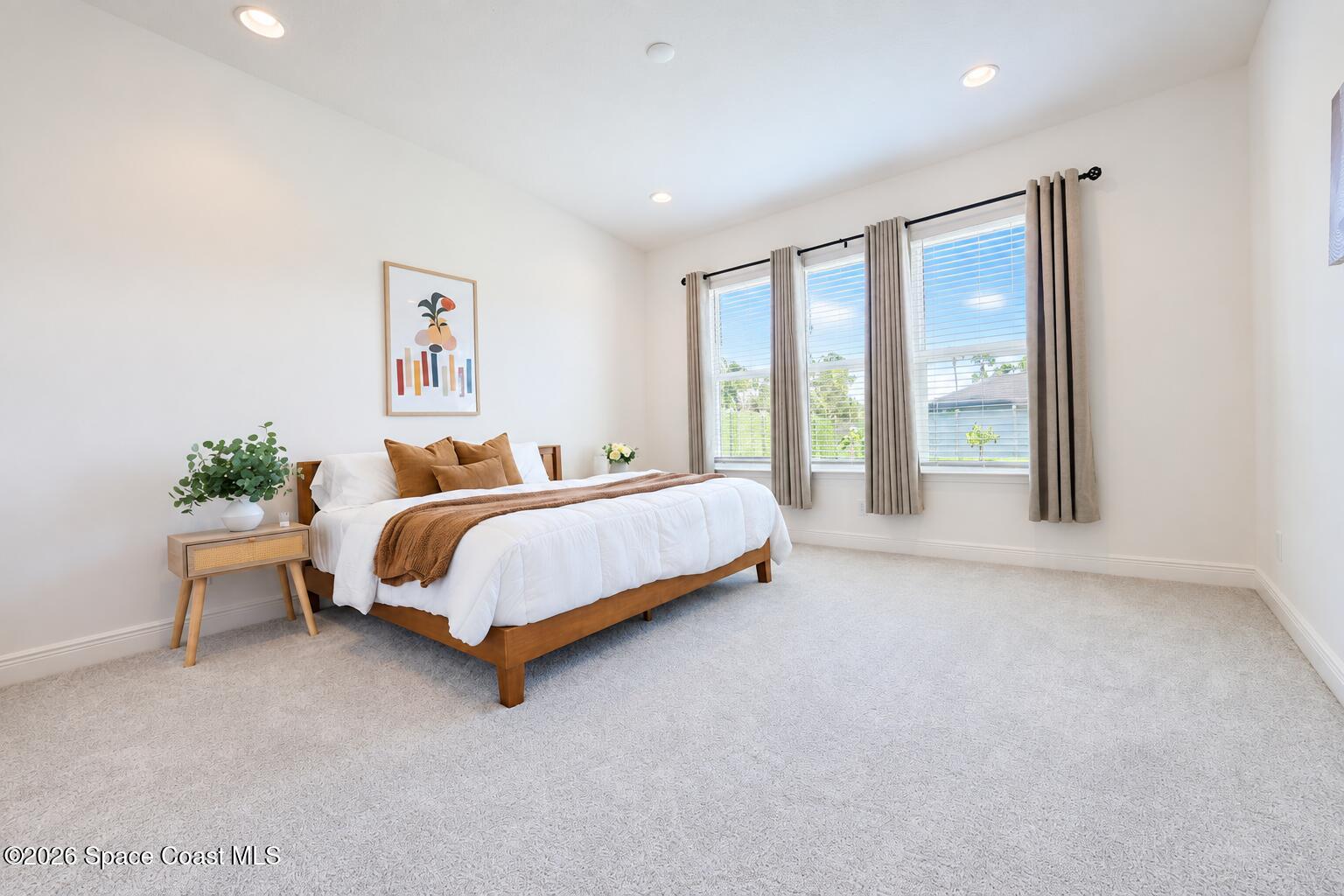 Staged bedroom with a wooden bed, white bedding, rust-colored accents, and three curtained windows.