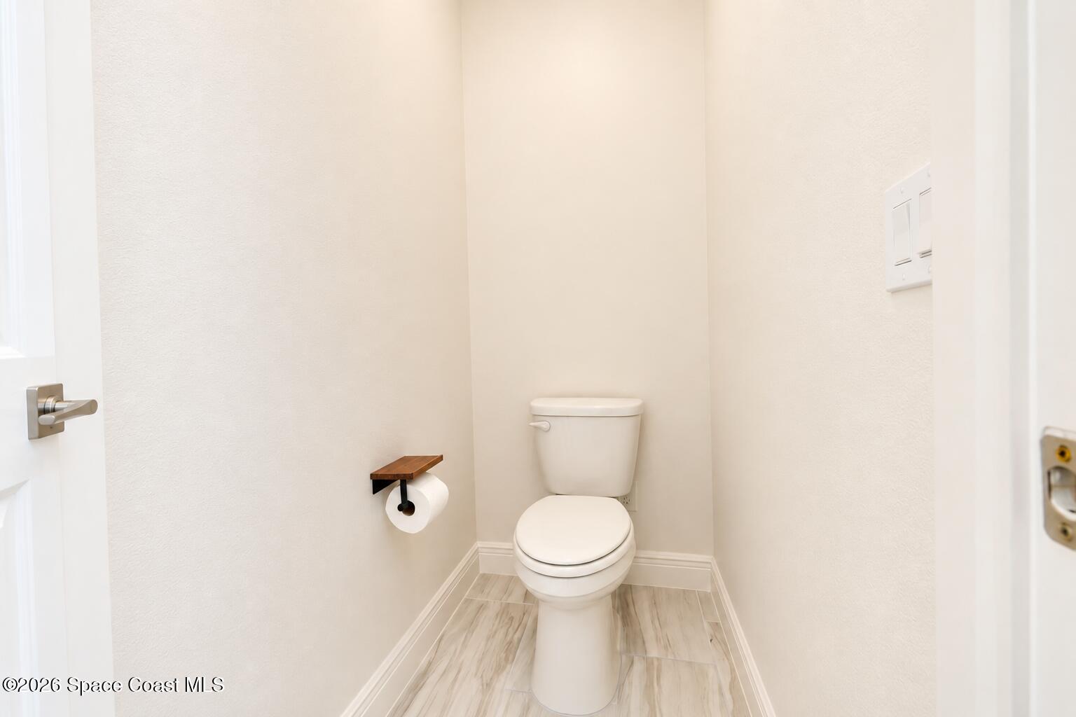 Small bathroom with a white toilet, wood toilet-paper holder, and light wood-look tile floor.