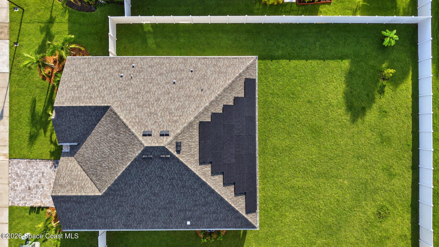 Aerial view of a house with rooftop solar panels and a fenced green lawn.