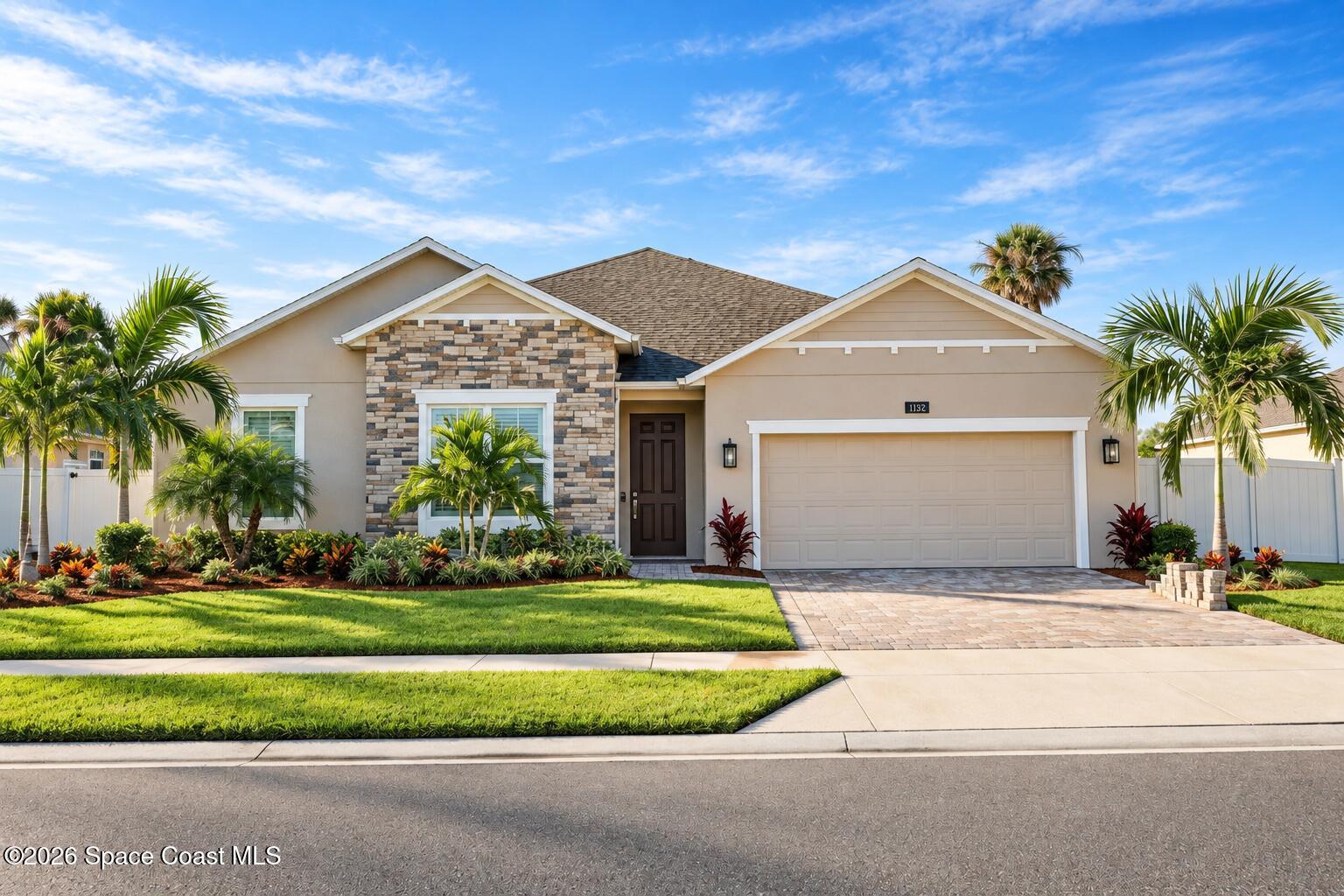 Single-story beige home with stone facade, two-car garage, and palm-lined landscaping.