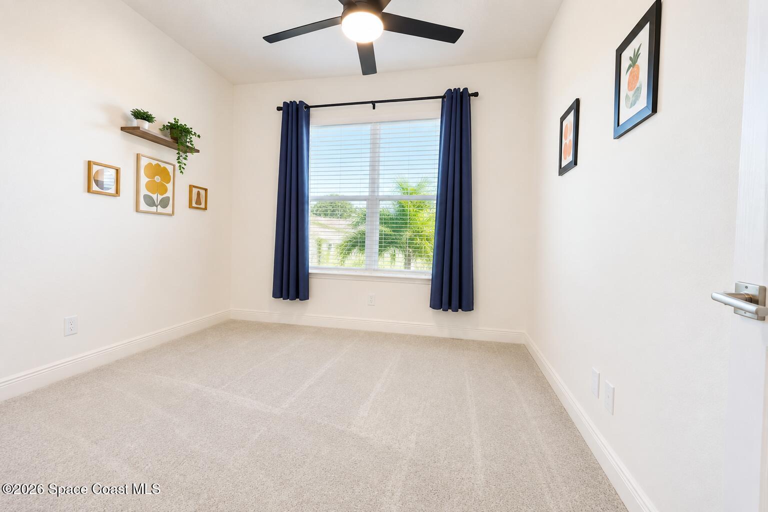 Empty carpeted bedroom with navy curtains, a ceiling fan, and palm trees visible through the window.