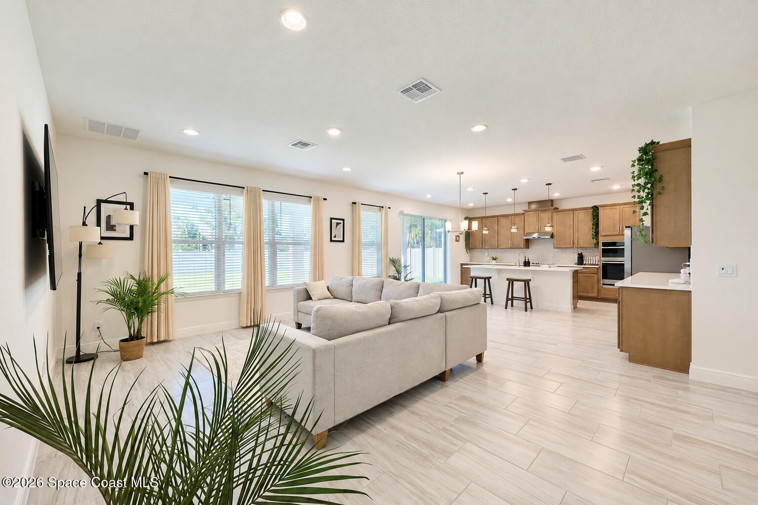 Open-plan living room and kitchen with a light sectional, large windows, and warm wood cabinetry.