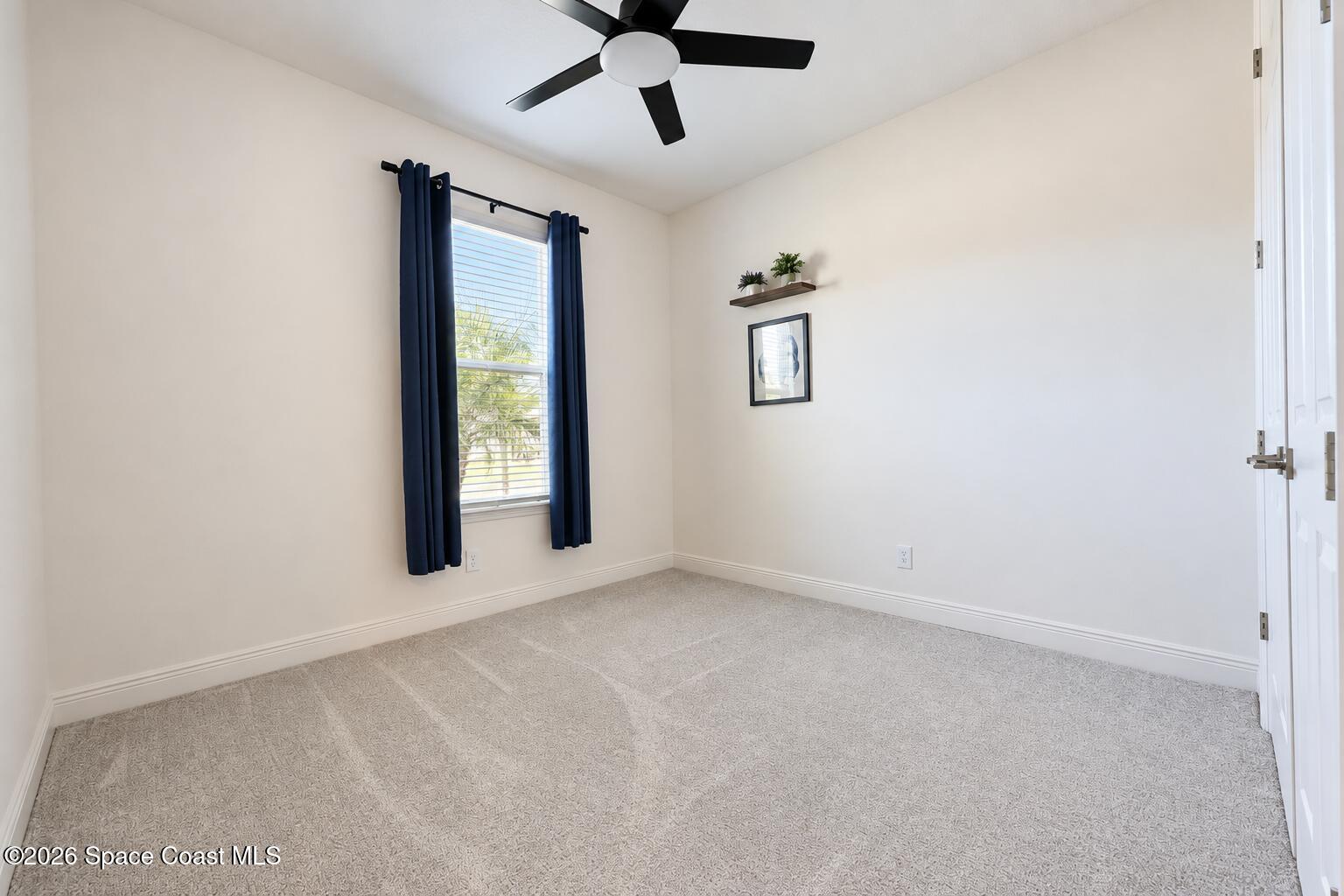Vacant carpeted bedroom with navy window curtains, a black ceiling fan, and minimal wall decor.